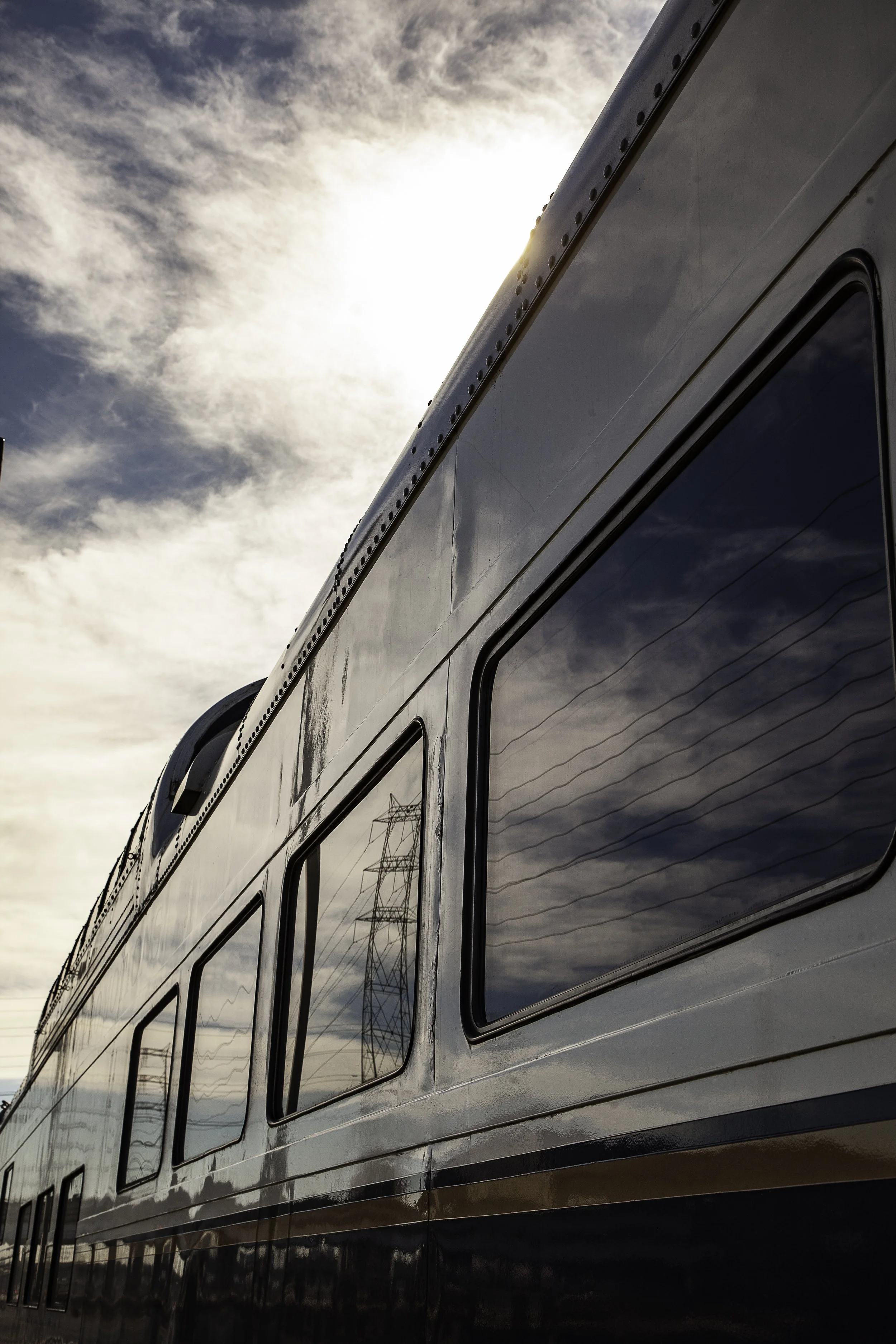Close-up of the upper part of a modern train with reflective windows, with an overcast sky and partly cloudy weather in the background.