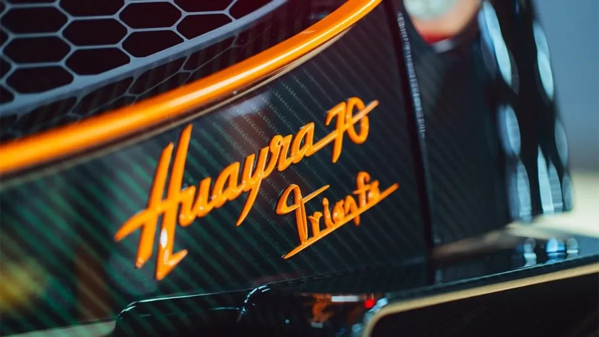 Close-up of a black race car with orange accents and the text "Hunayaga Triote" in orange script on the side.