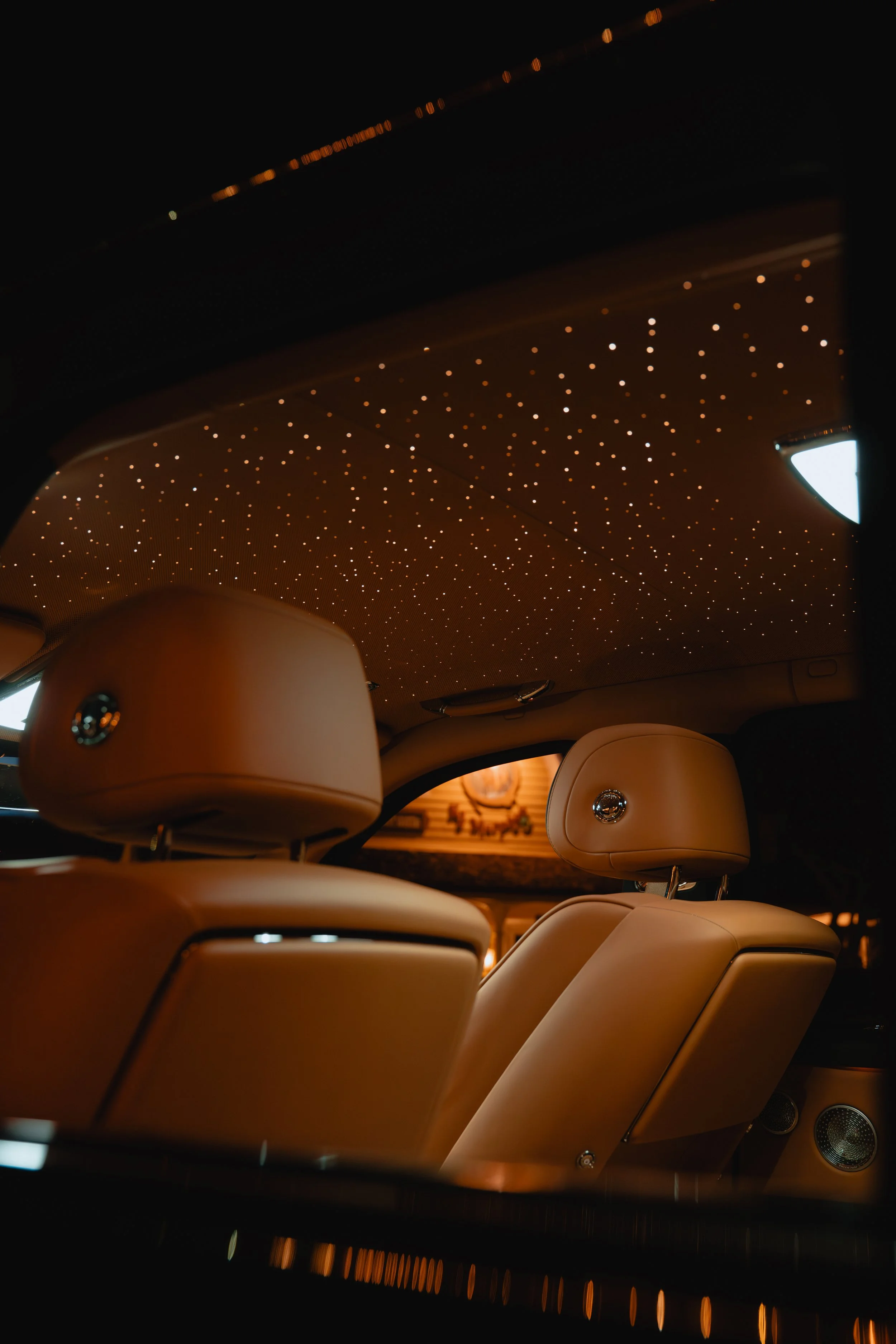 Luxury car interior with tan leather seats and a starry sky ceiling feature of small LED lights, creating a galaxy effect.