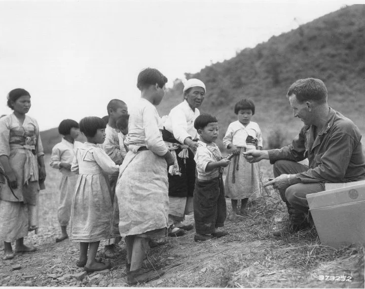 Korean War SC Coll Box 1, RG6s-KWP.27 1st LT William Millward of Baltimore, Md, Civil Assistant Officer, 5th Cavalry Regiment, 1st Cavalry Division, distributes candy to Korean children at a refugee collecting point in Western Korea.