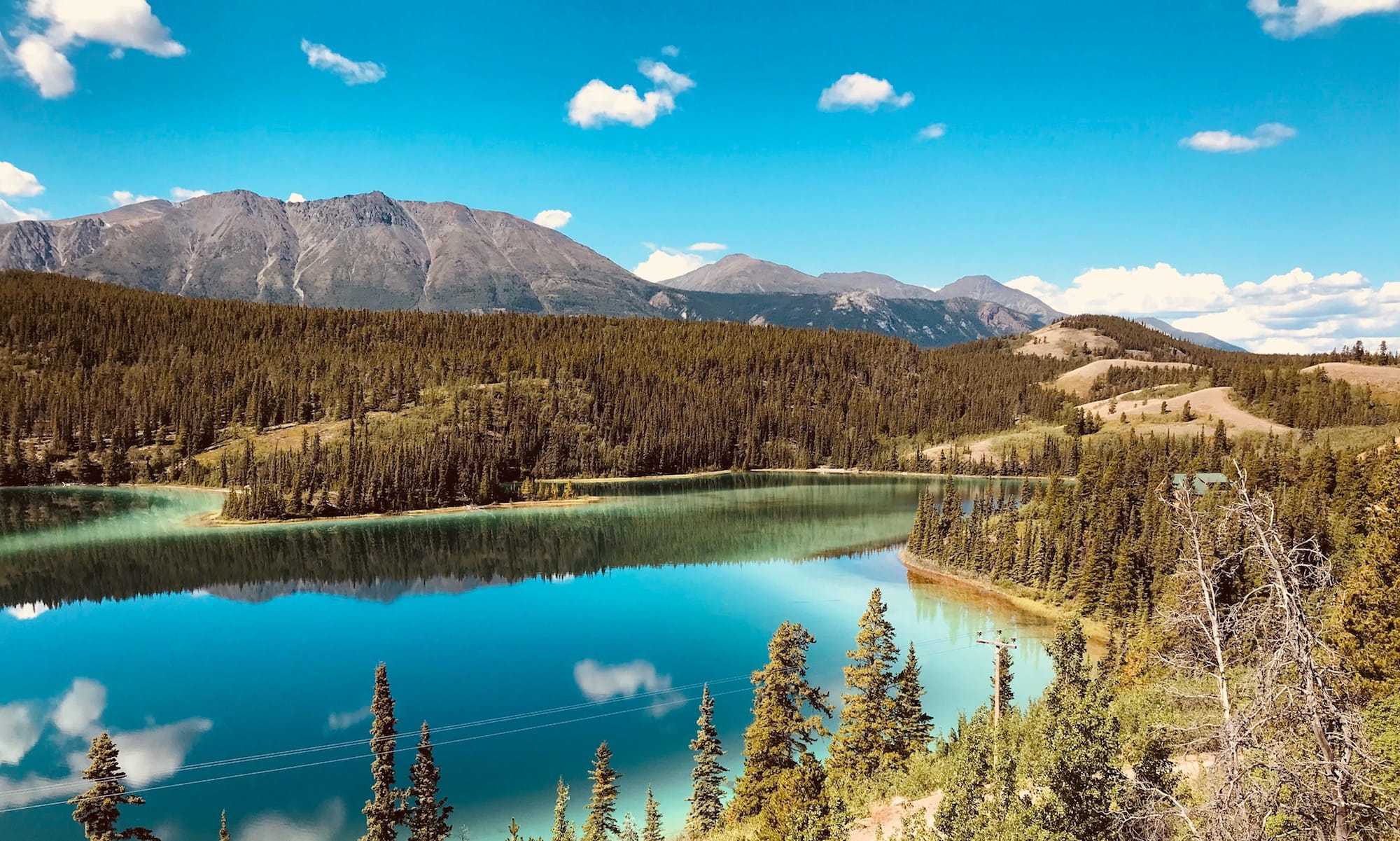 Photo of a gorgeous turquoise and teal lake with trees ringing it and mountains in the background.jpg