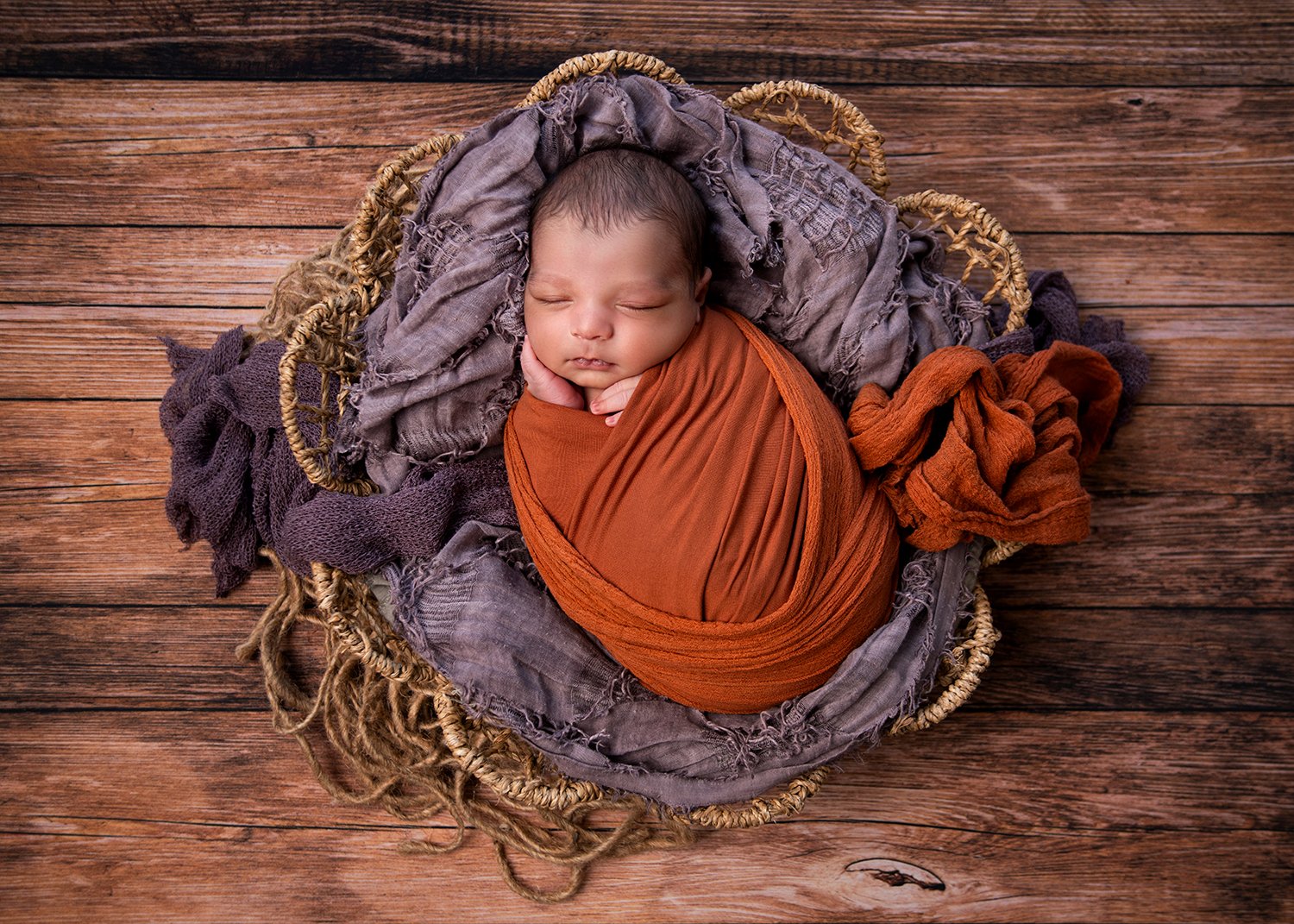 Baby sleeping on basket wearing burnt orange and purple