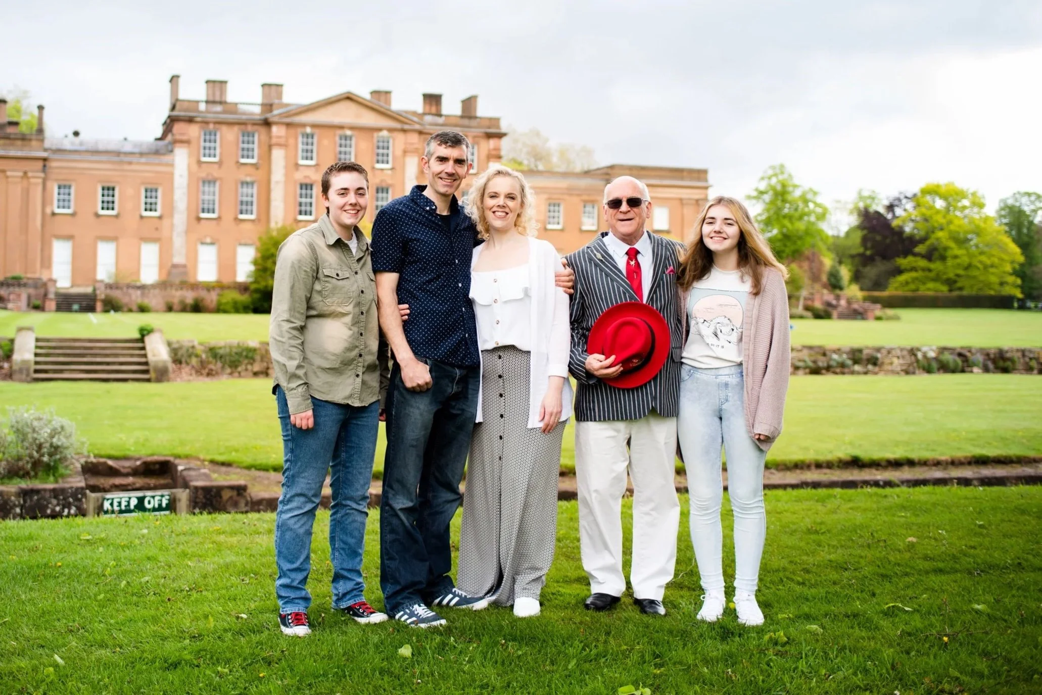 Family of five standing on a lawn in front of a large historic building, smiling and posing for a photo.