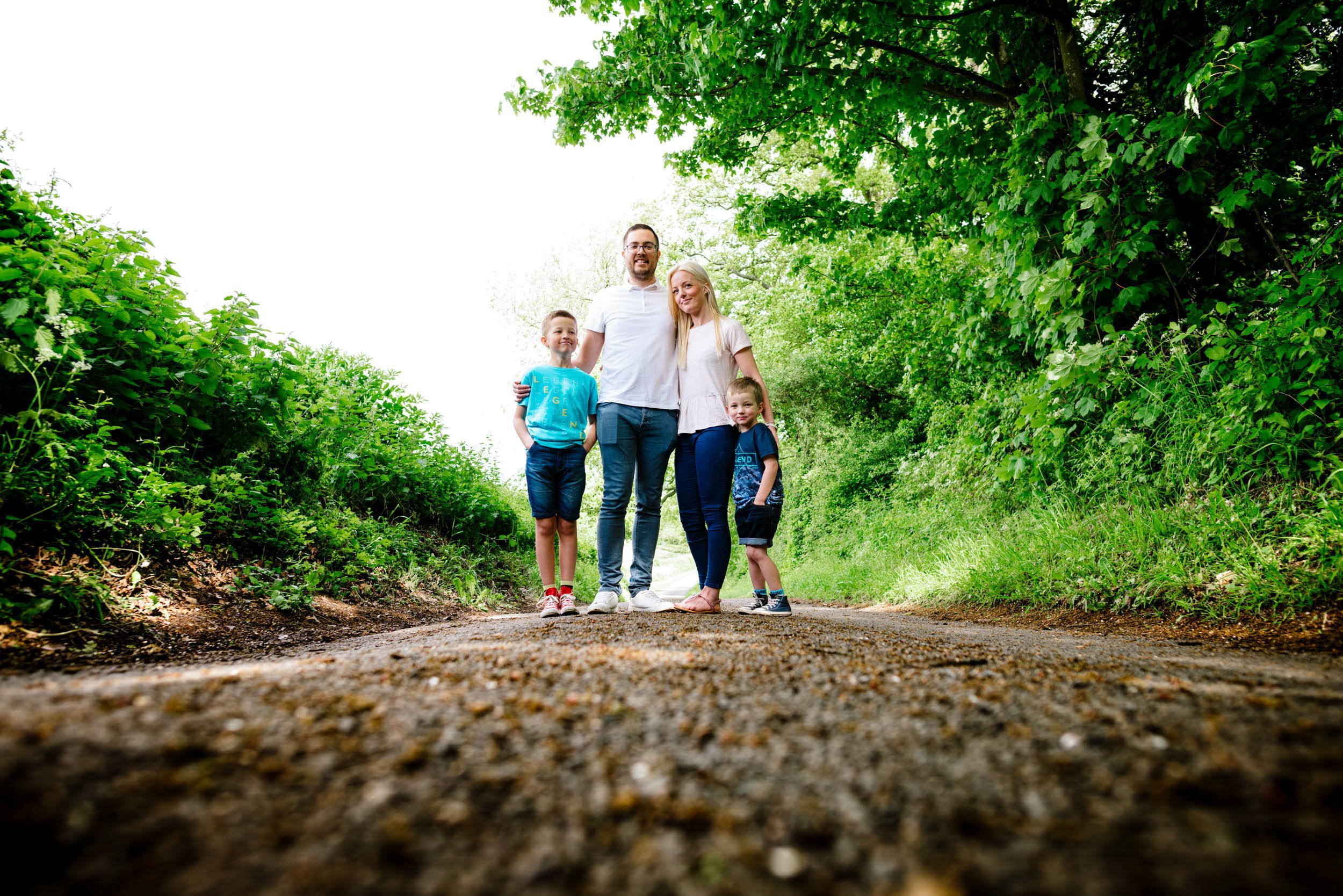 A family of four standing on a dirt path surrounded by lush green trees and bushes.