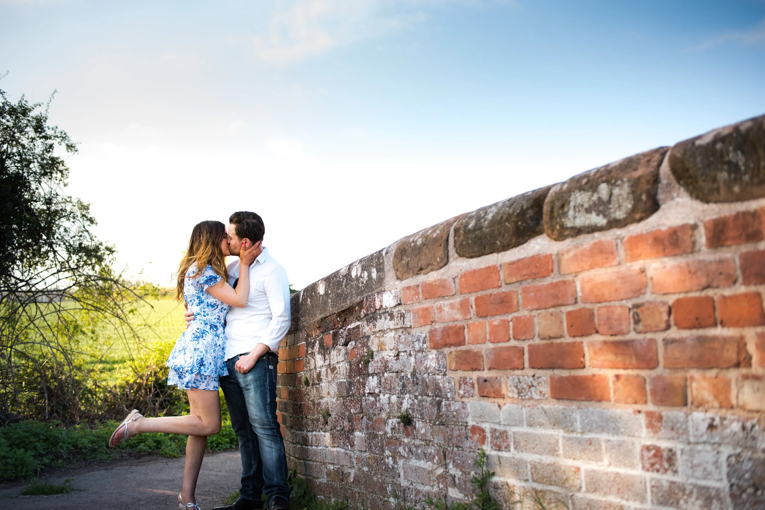 a couple kissing near a brick wall in an outdoor setting during daytime