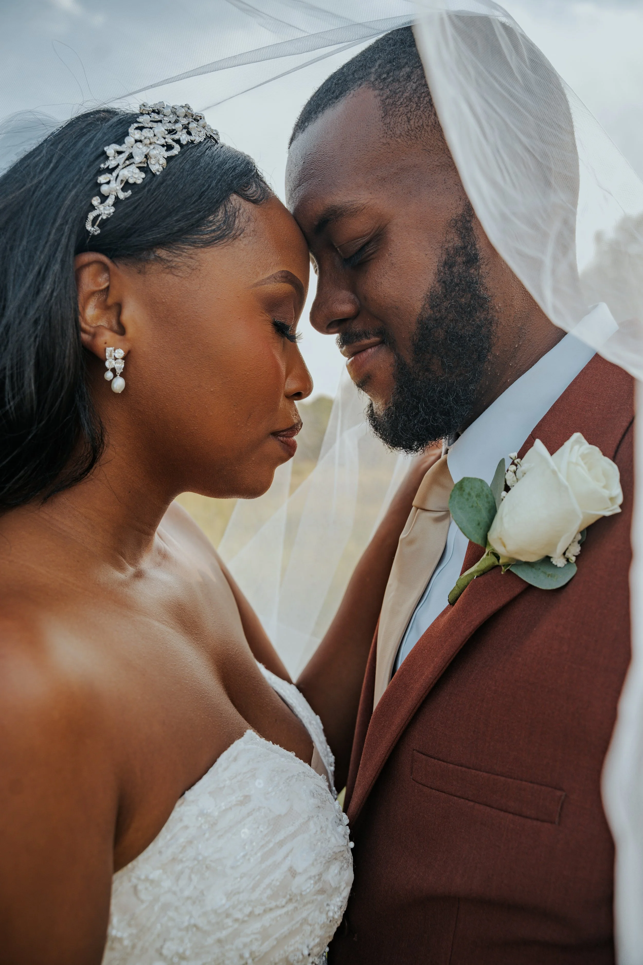 A bride and groom with their foreheads touching under a wedding veil, eyes closed, sharing an intimate moment.