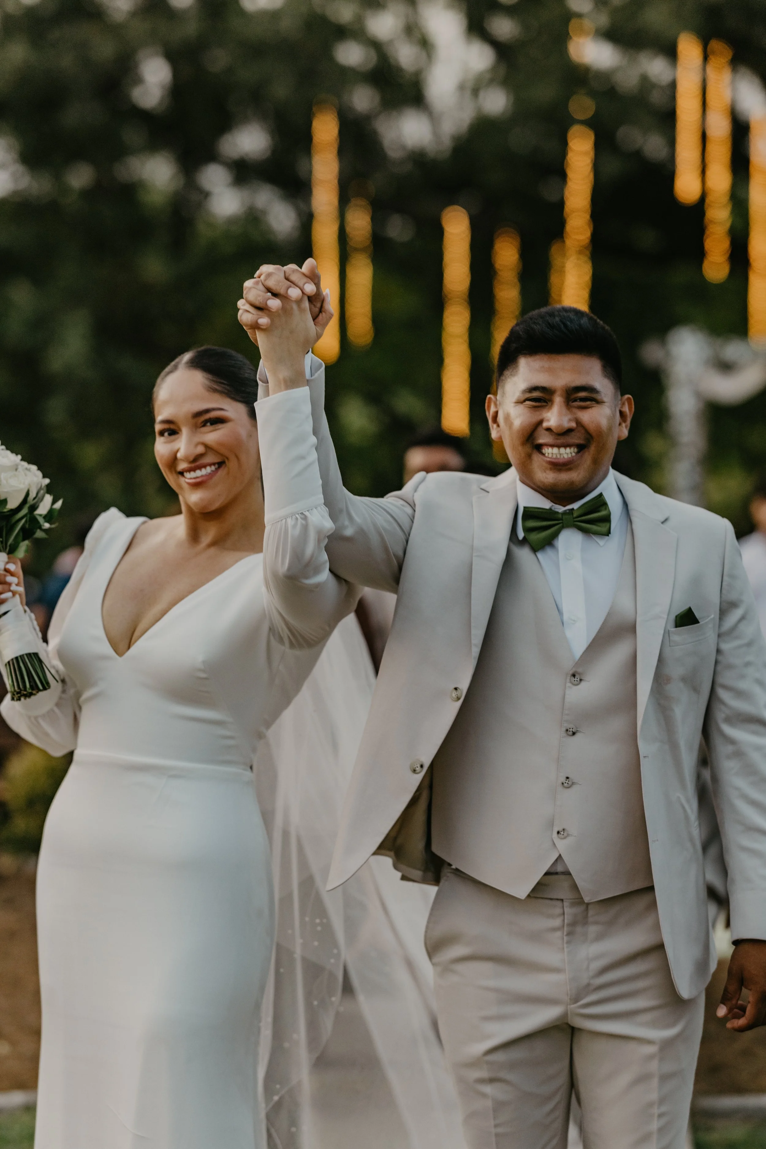 A happy bride and groom holding hands and smiling at their wedding celebration outdoors.