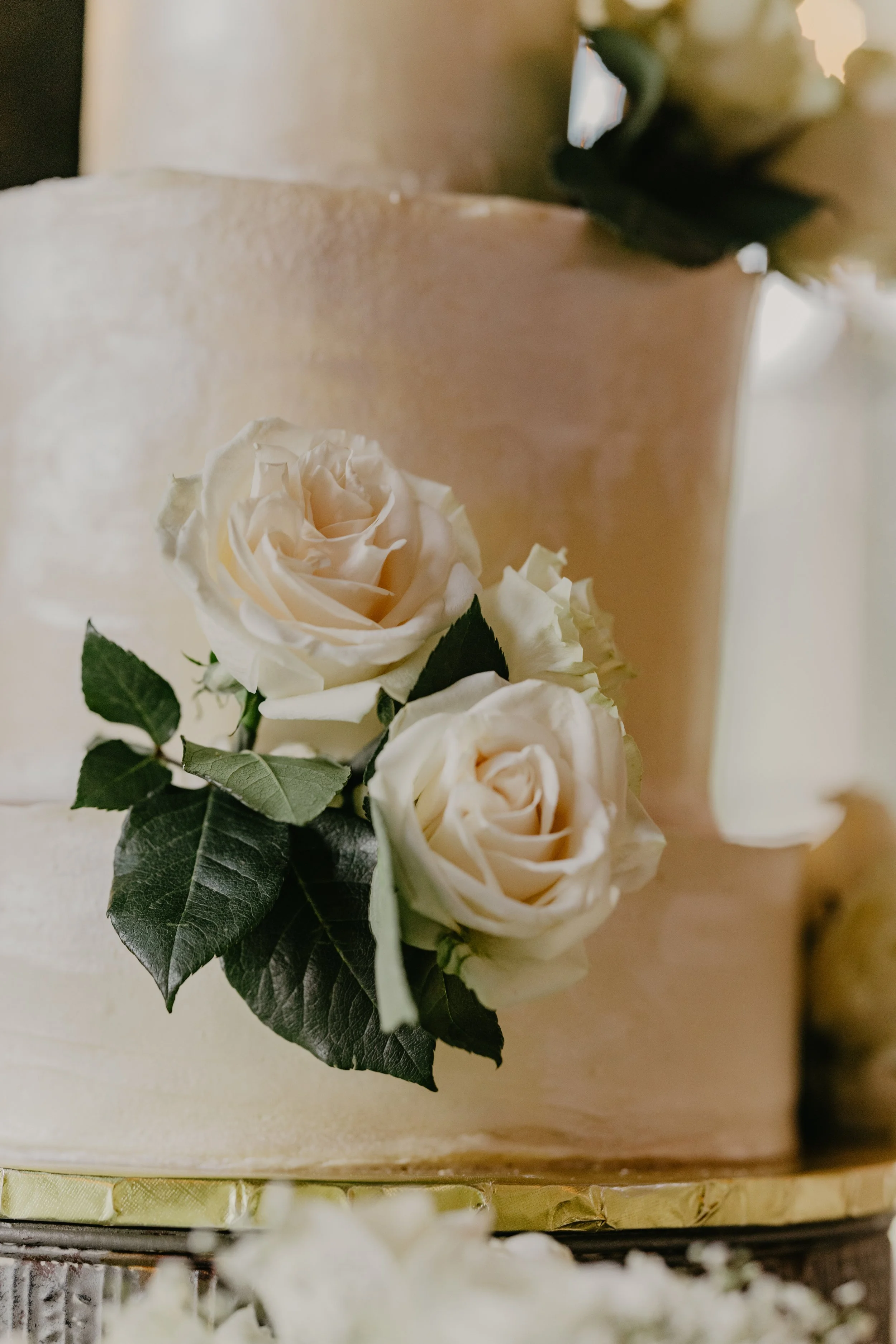 Close-up of a wedding cake decorated with white roses and green leaves.