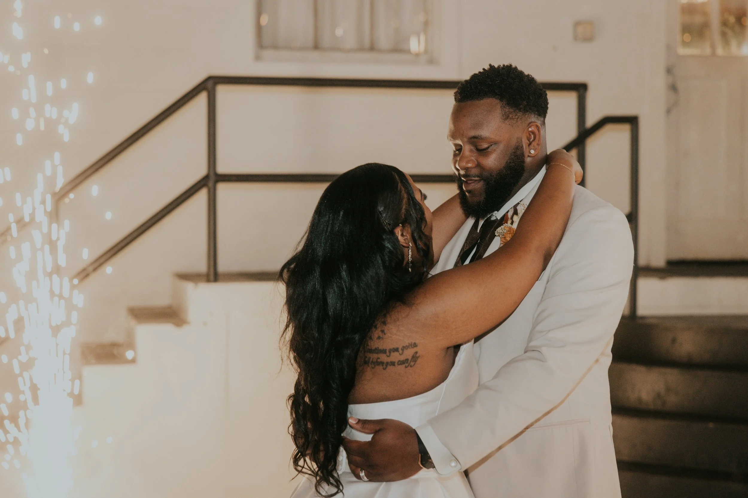 A couple is dancing closely at their wedding reception, with the bride in a white dress and the groom in a white tuxedo jacket.