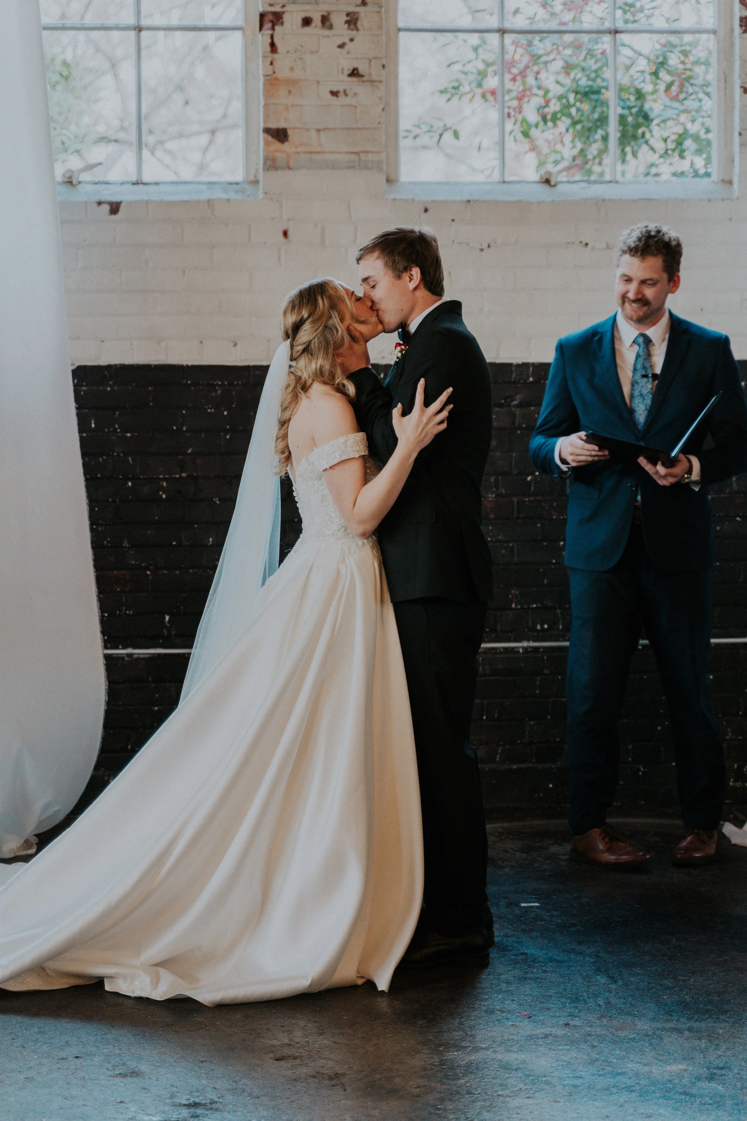 Bride and groom sharing a kiss during their wedding ceremony, with officiant standing nearby.