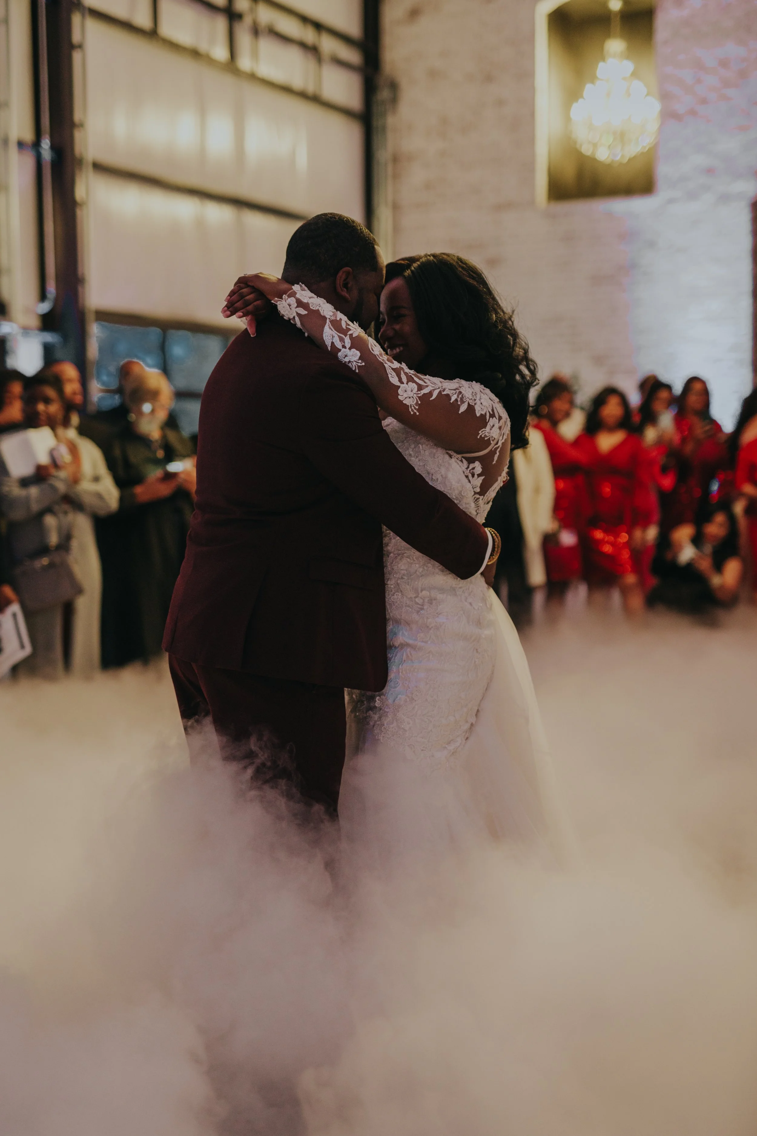 A newlywed couple sharing their first dance under a cloud of fog surrounded by wedding guests.