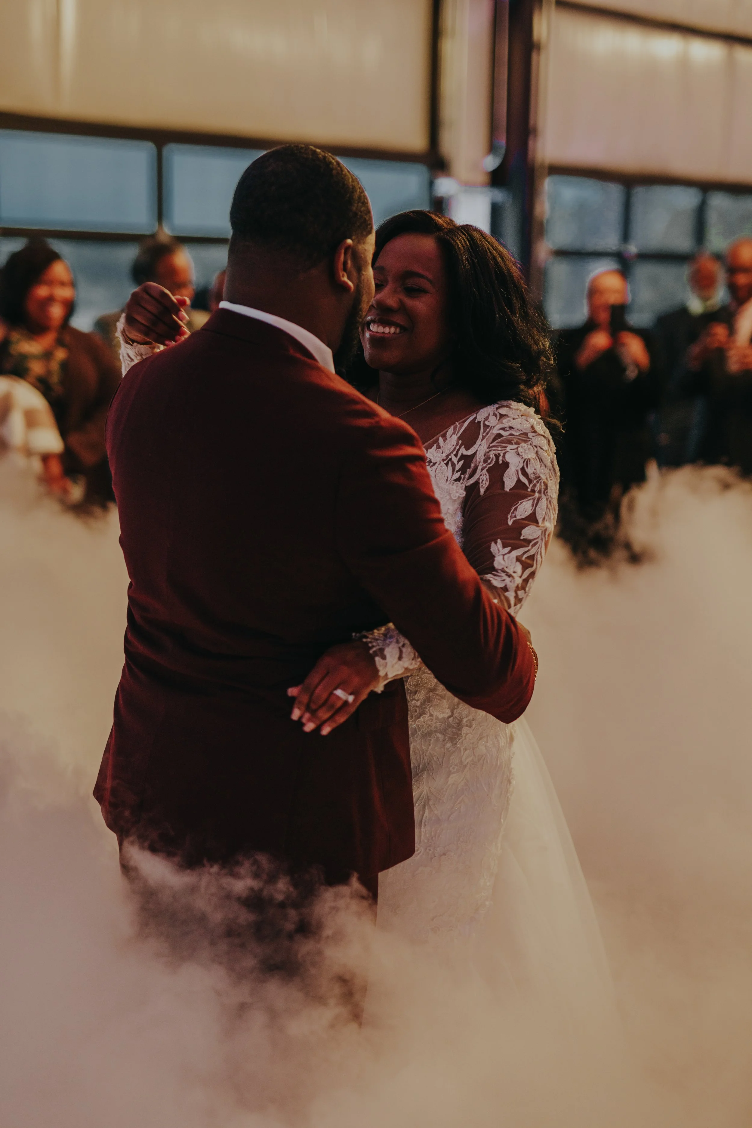Bride and groom dancing at their wedding, surrounded by guests, with a misty dance floor.