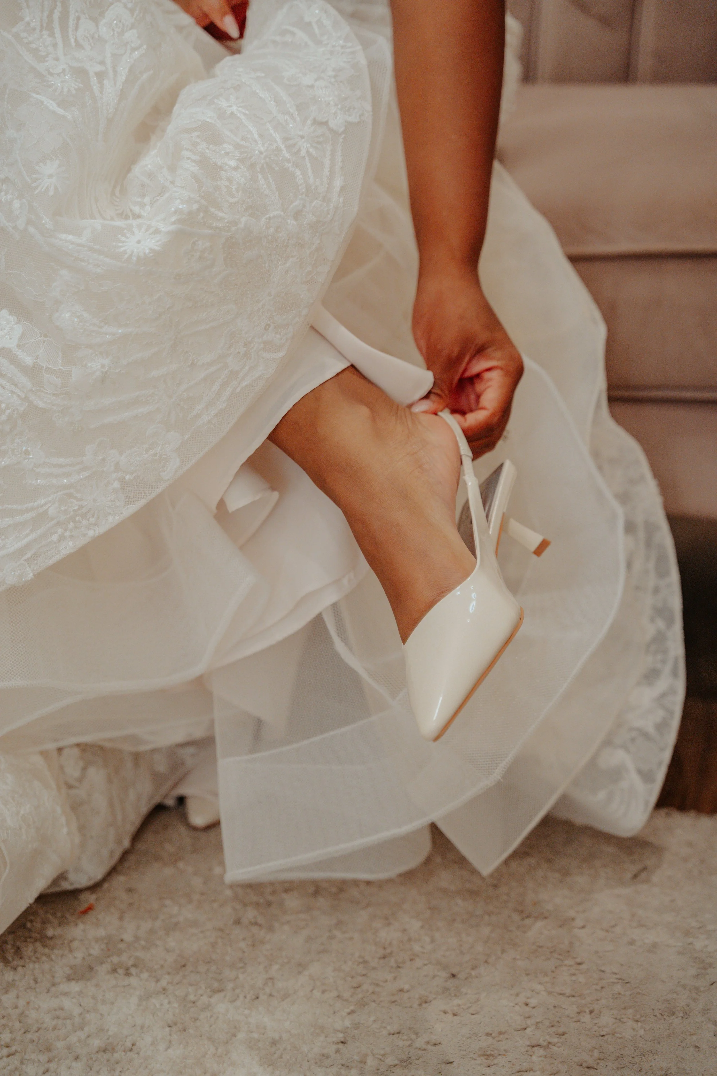 A woman in a bridal dress is putting on a white high-heeled shoe.