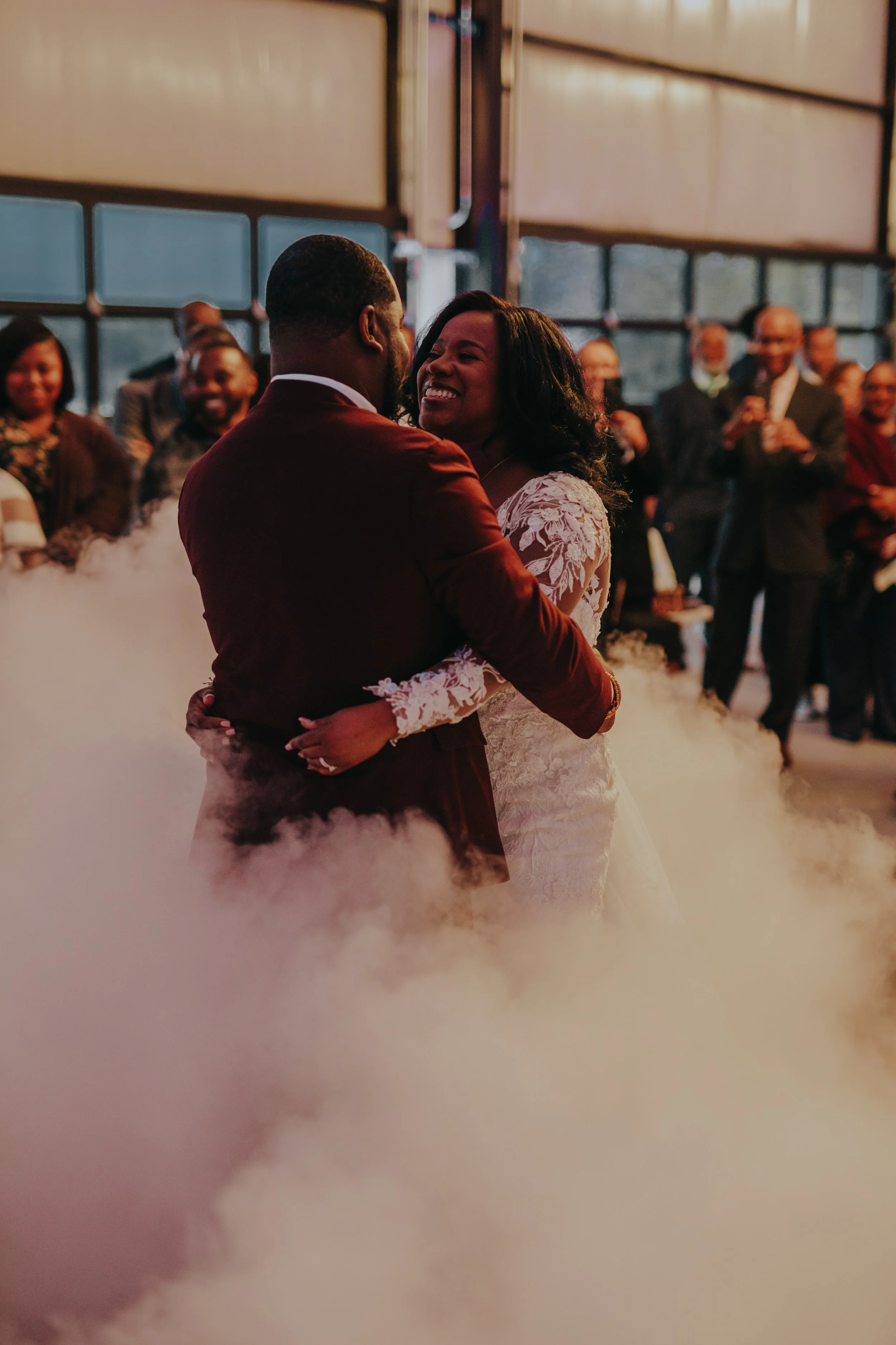 A bride and groom sharing their first dance surrounded by guests, with fog on the dance floor