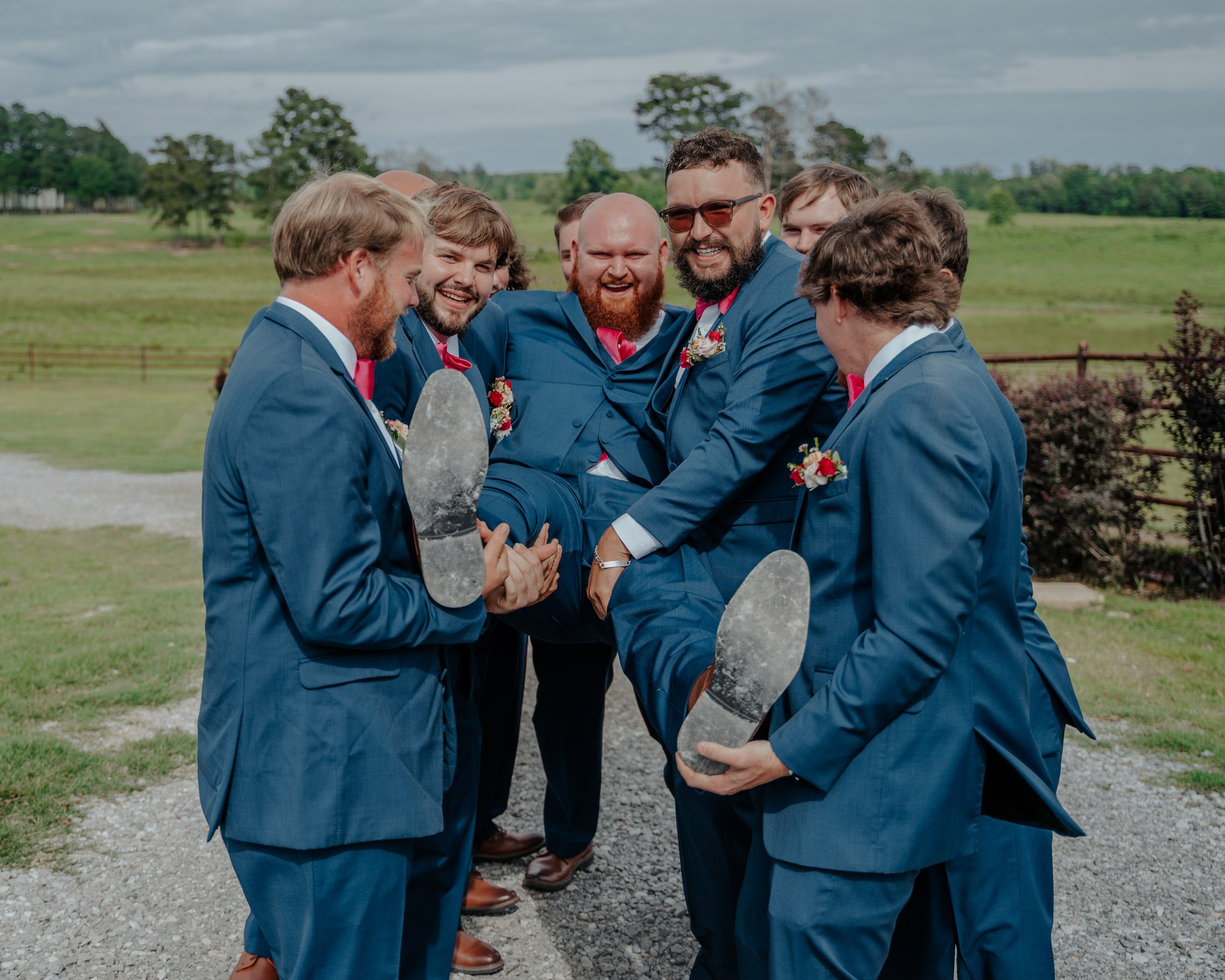 A group of men in blue suits celebrating outdoors, with one man being lifted by others, all smiling and enjoying a joyful moment.