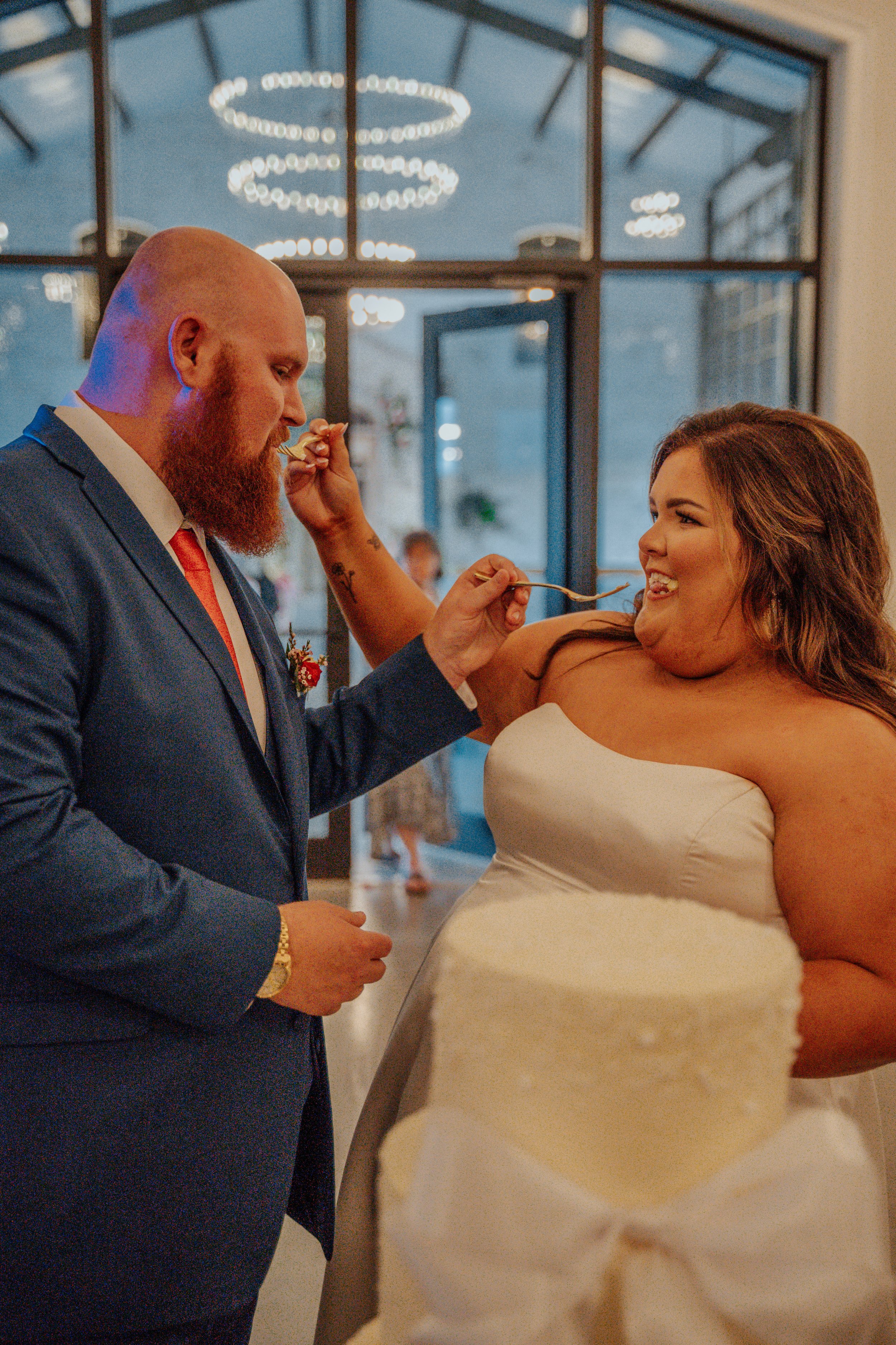 A newlywed couple sharing a humorous moment during their wedding reception, with the bride feeding the groom cake.