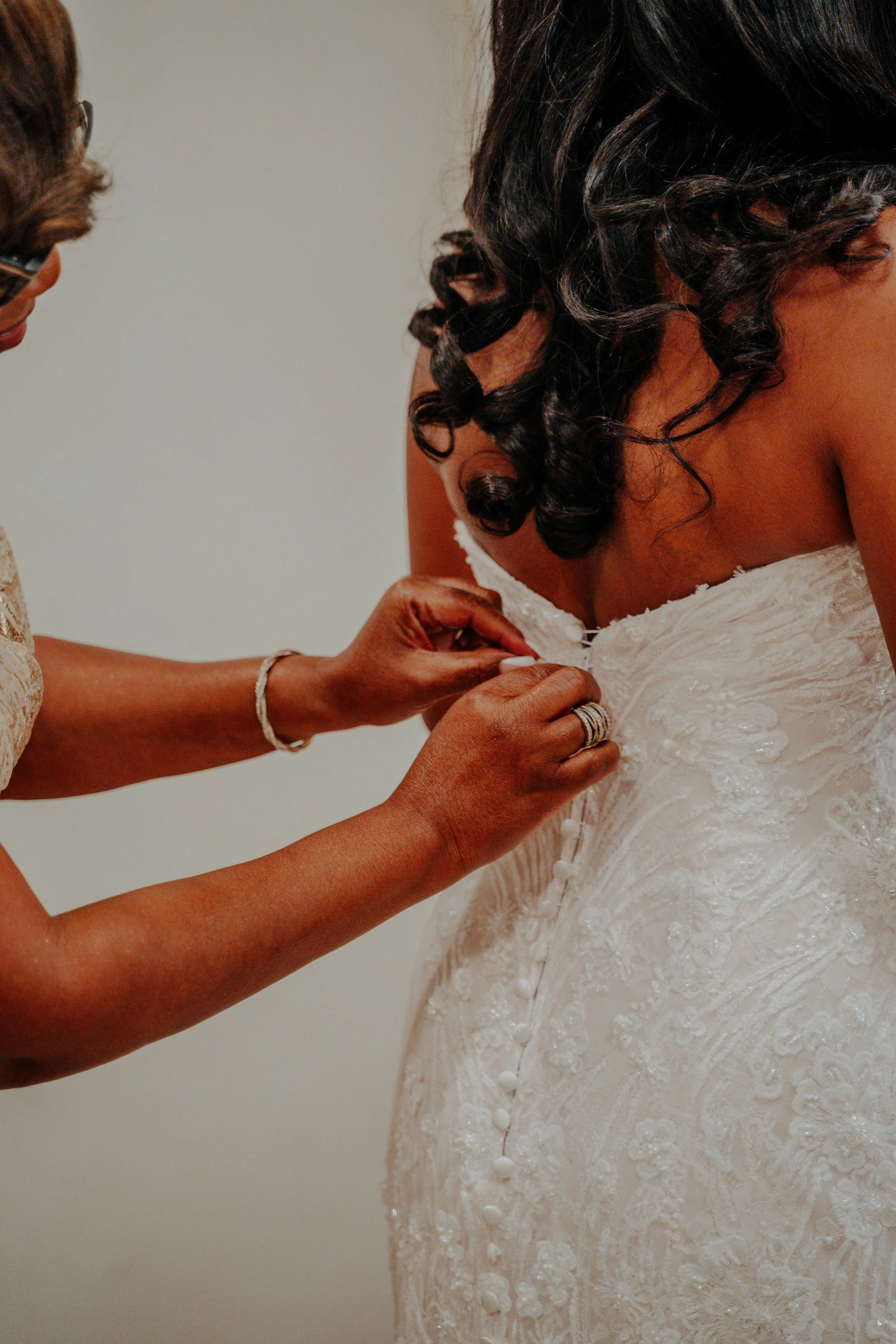 A woman helping a bride zip up the back of her wedding dress.