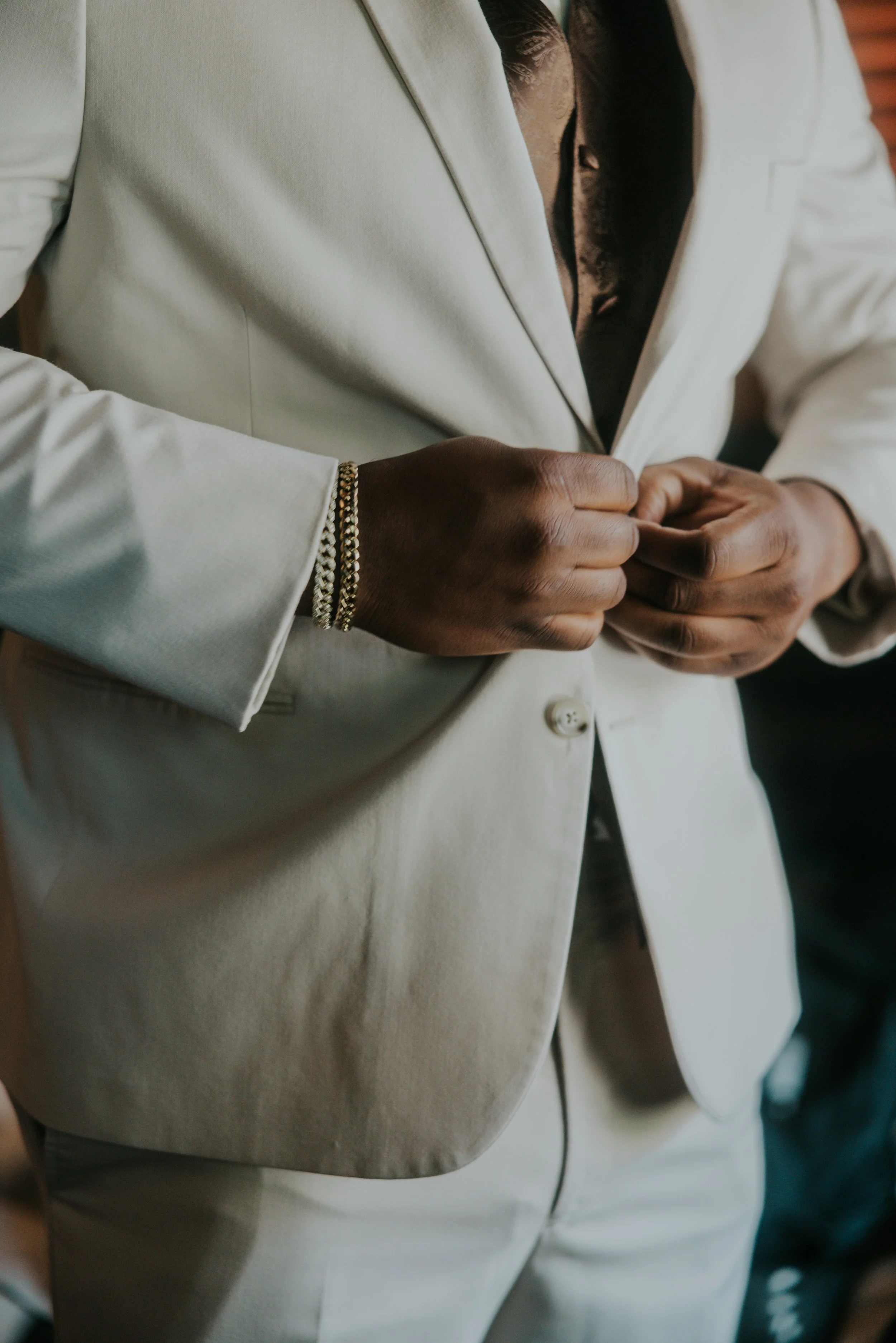 Person adjusting a white suit jacket, wearing gold bracelets on the left wrist.