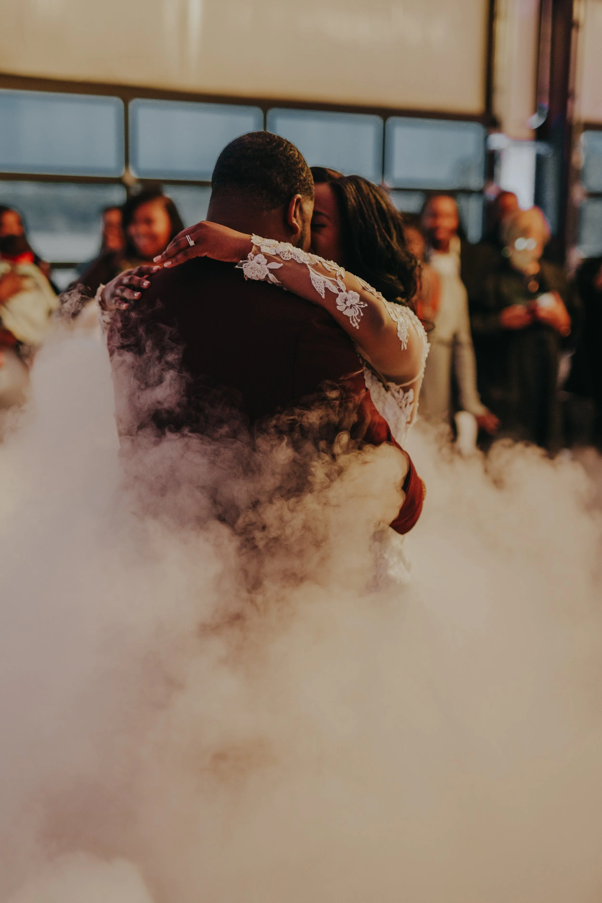 A newlywed couple's first dance at their wedding, with smoke or fog surrounding them and guests watching.