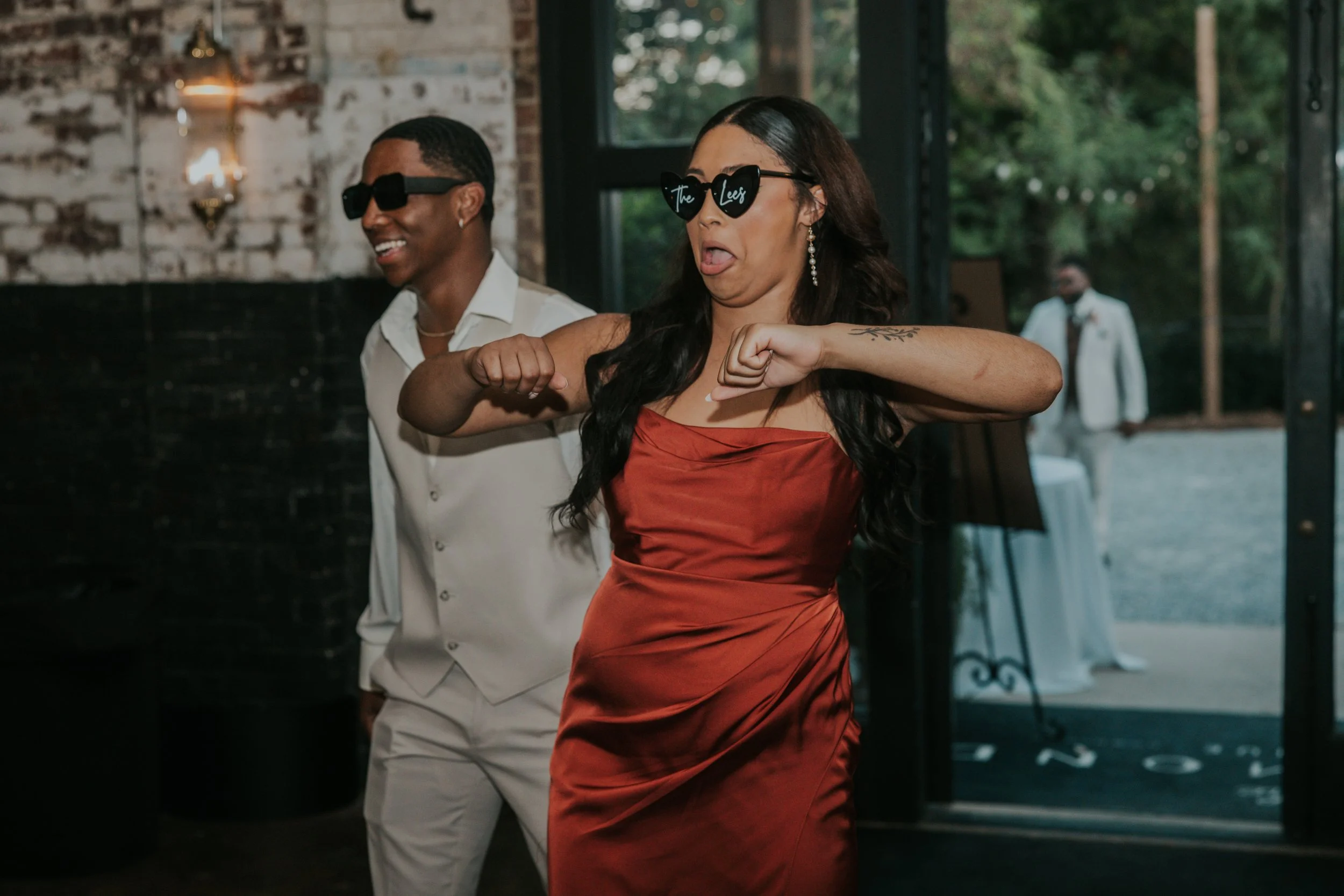 Two women dancing and enjoying themselves at a party, wearing sunglasses, with one woman making a funny face and the other smiling.