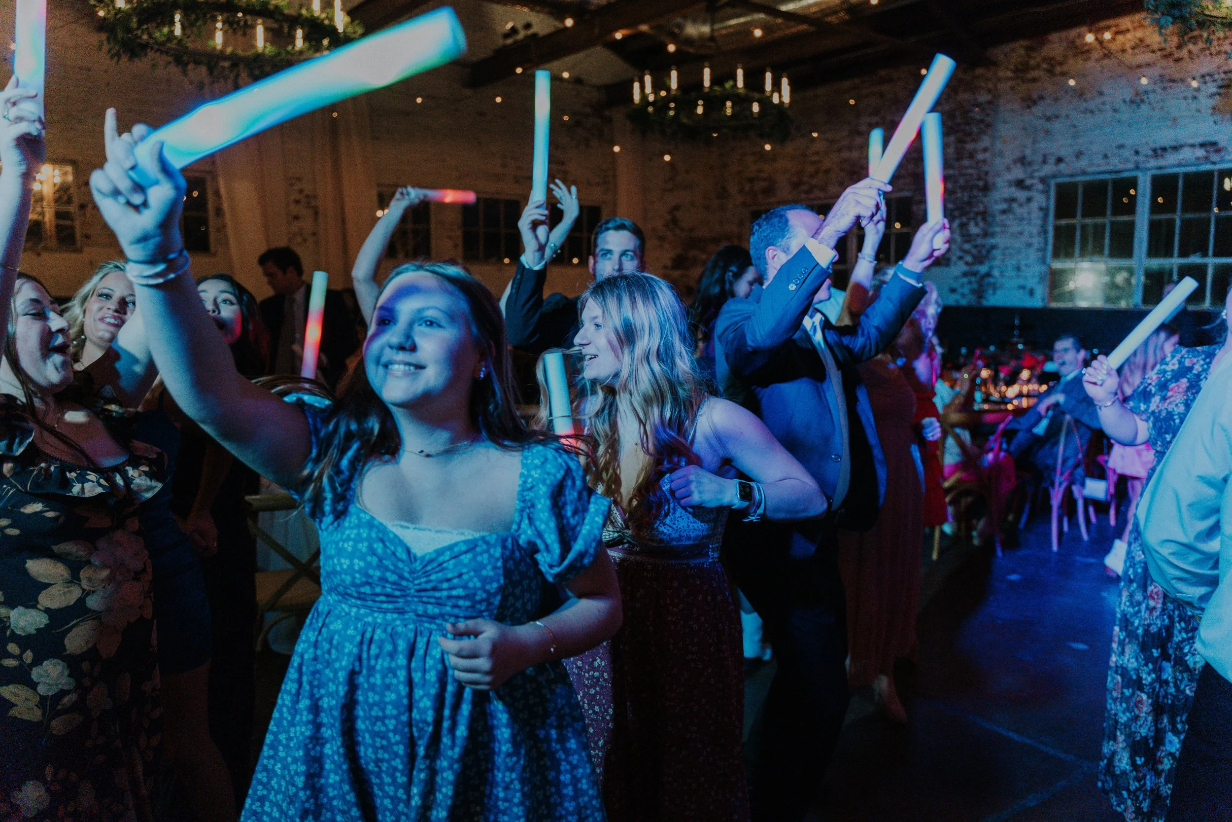 People dancing and enjoying themselves at a party with glow sticks in a dimly lit, festive indoor setting.