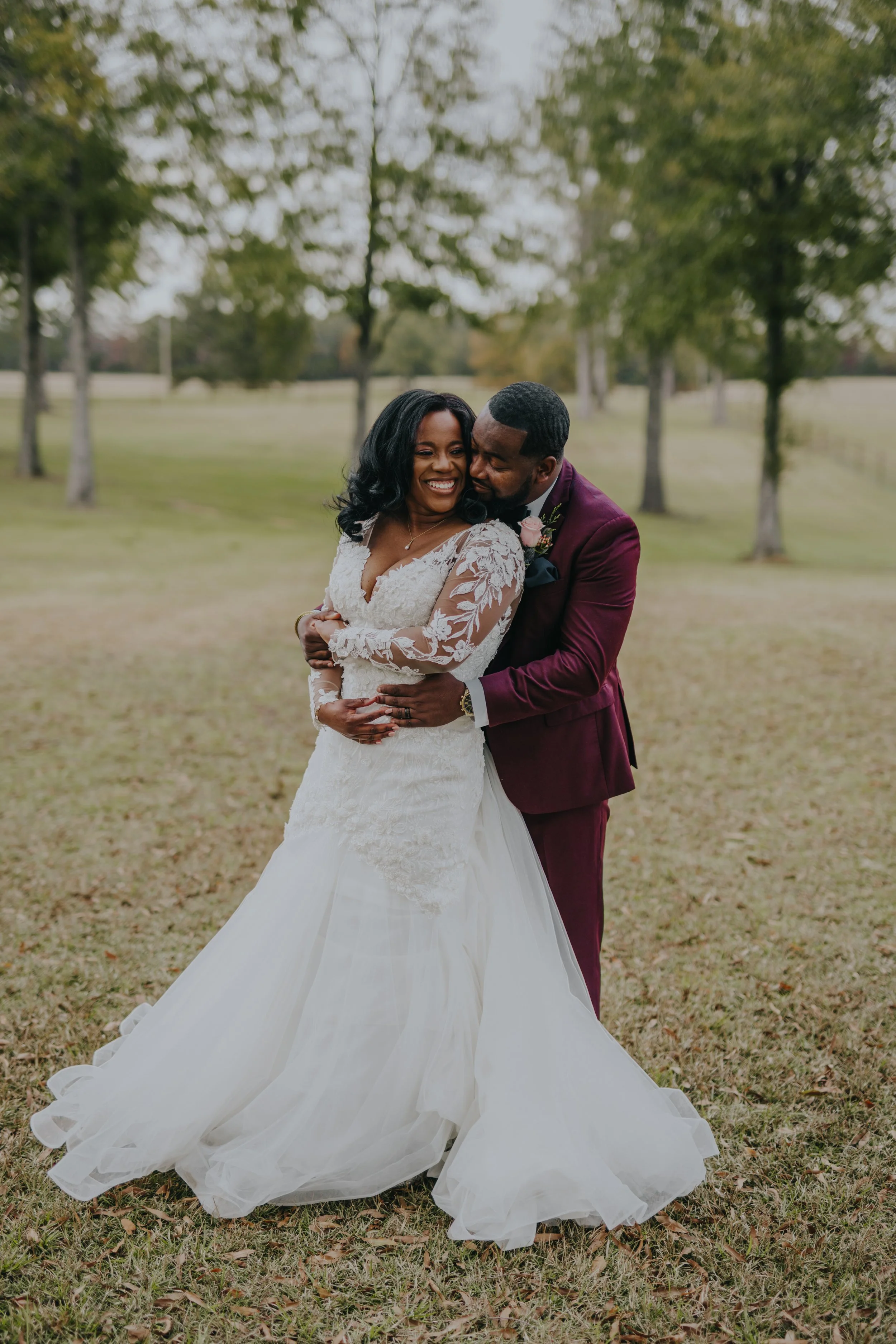A happy bride and groom hugging outdoors in a park with trees and grass.