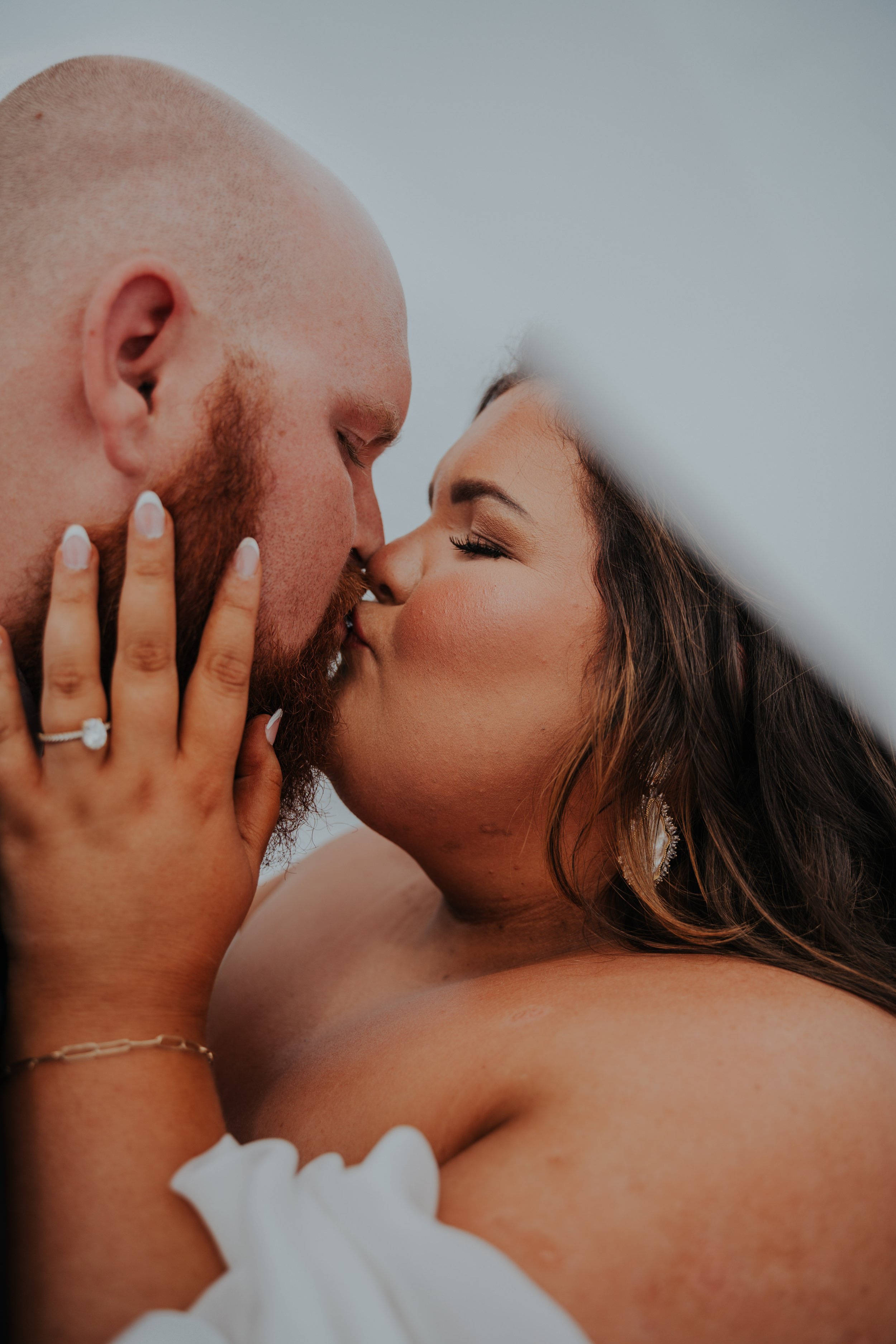 Close-up of a couple kissing, with the woman's hand resting on the man's face, showing an engagement ring.