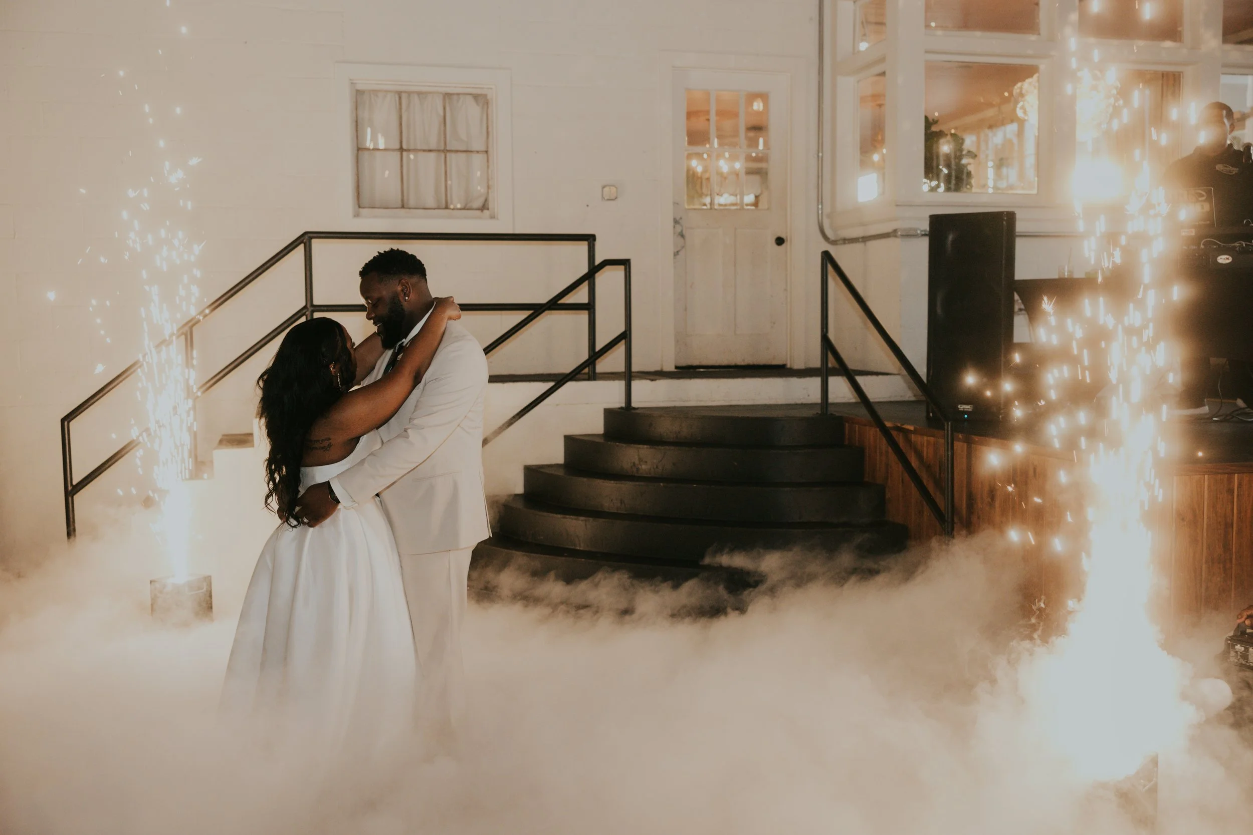A bride and groom dancing in a wedding reception with sparklers and fog effects.