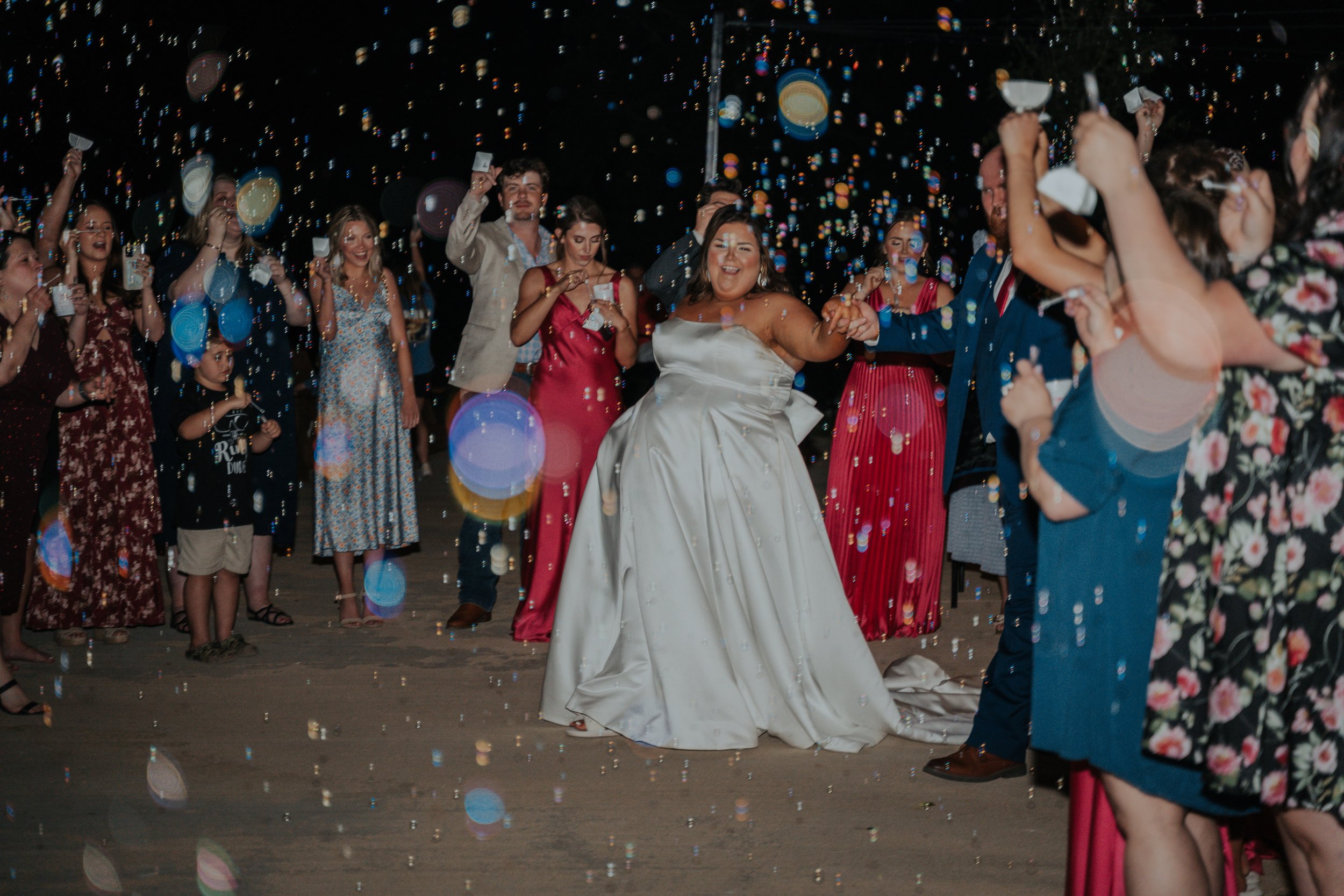 Bride dancing in a white wedding gown surrounded by guests celebrating at a nighttime wedding reception with confetti.