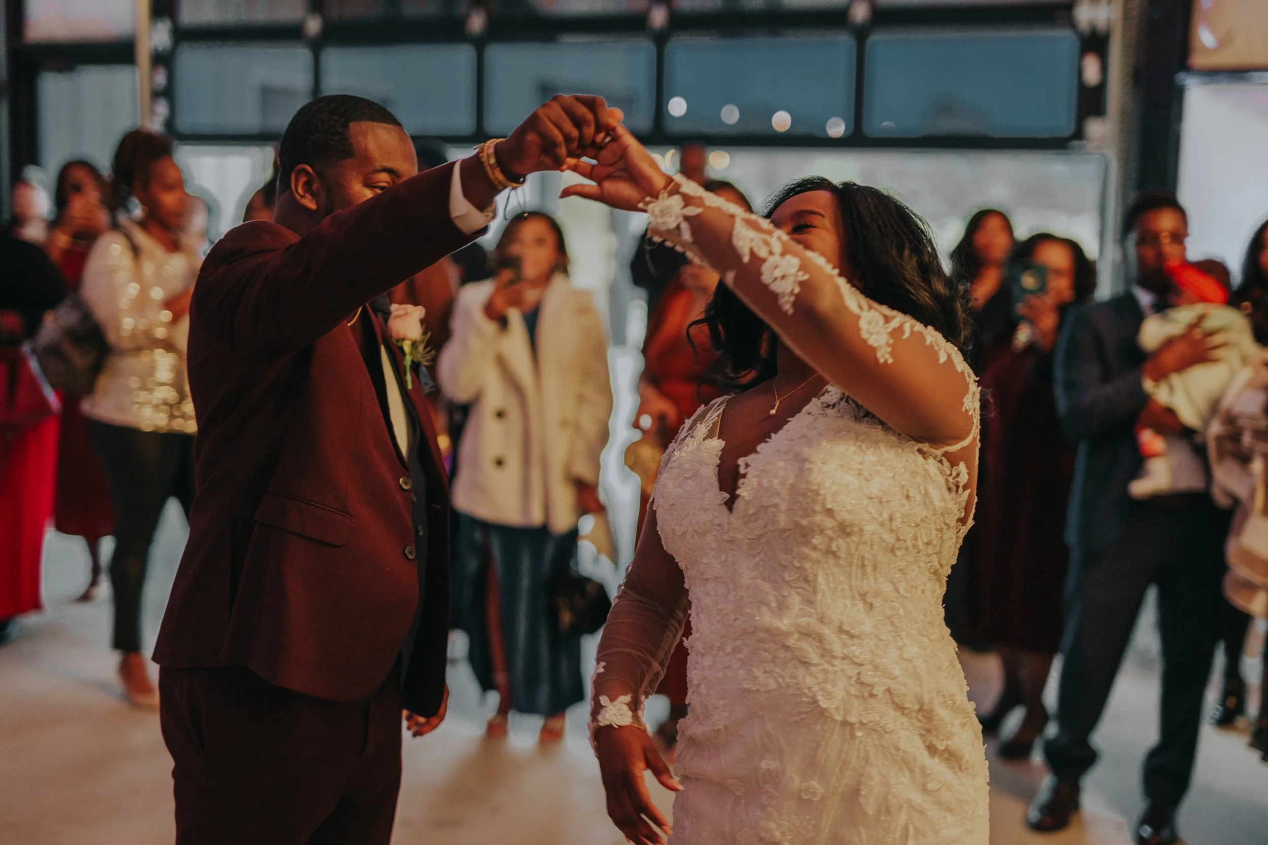 A newlywed couple dancing at their wedding reception with guests watching in the background.