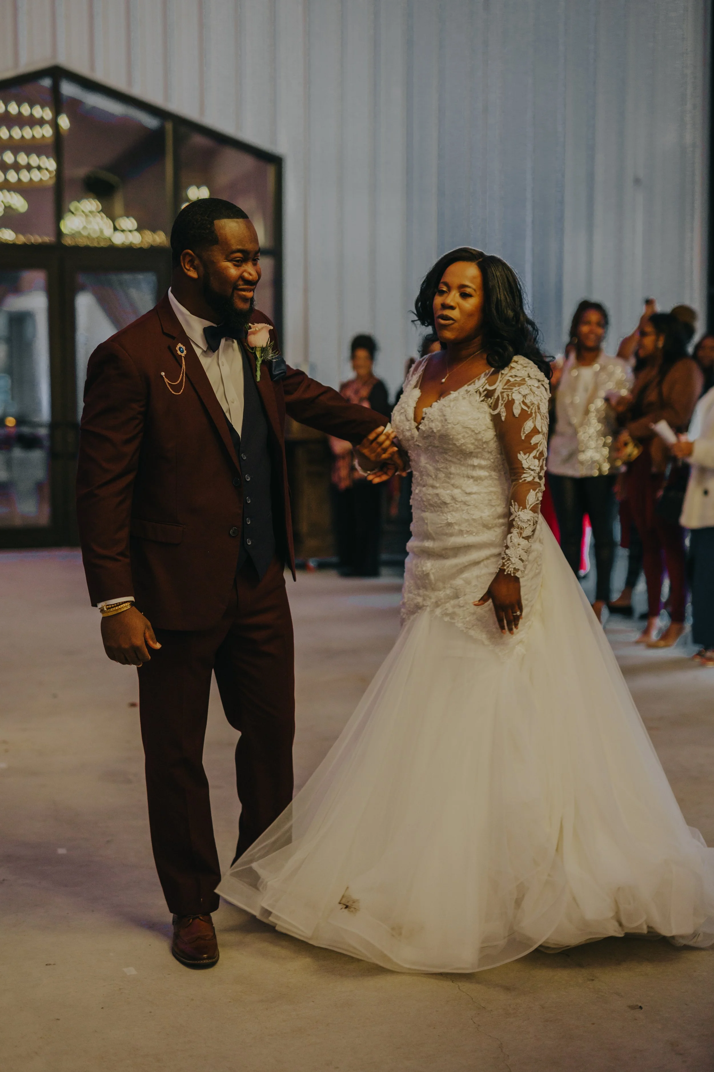 A groom and bride are dancing at their wedding reception with guests in the background.