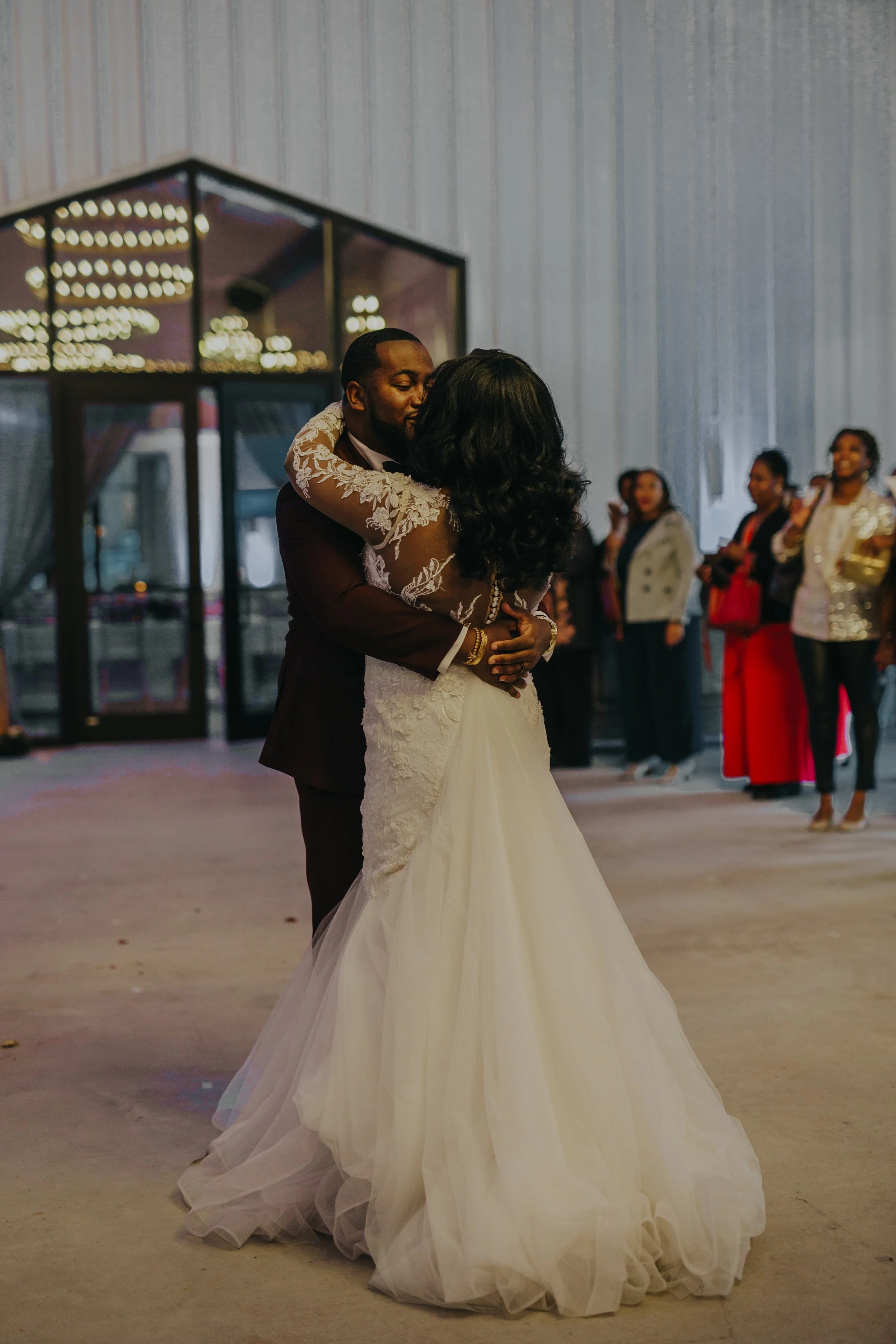 A bride and groom sharing their first dance at a wedding reception with guests watching in the background.