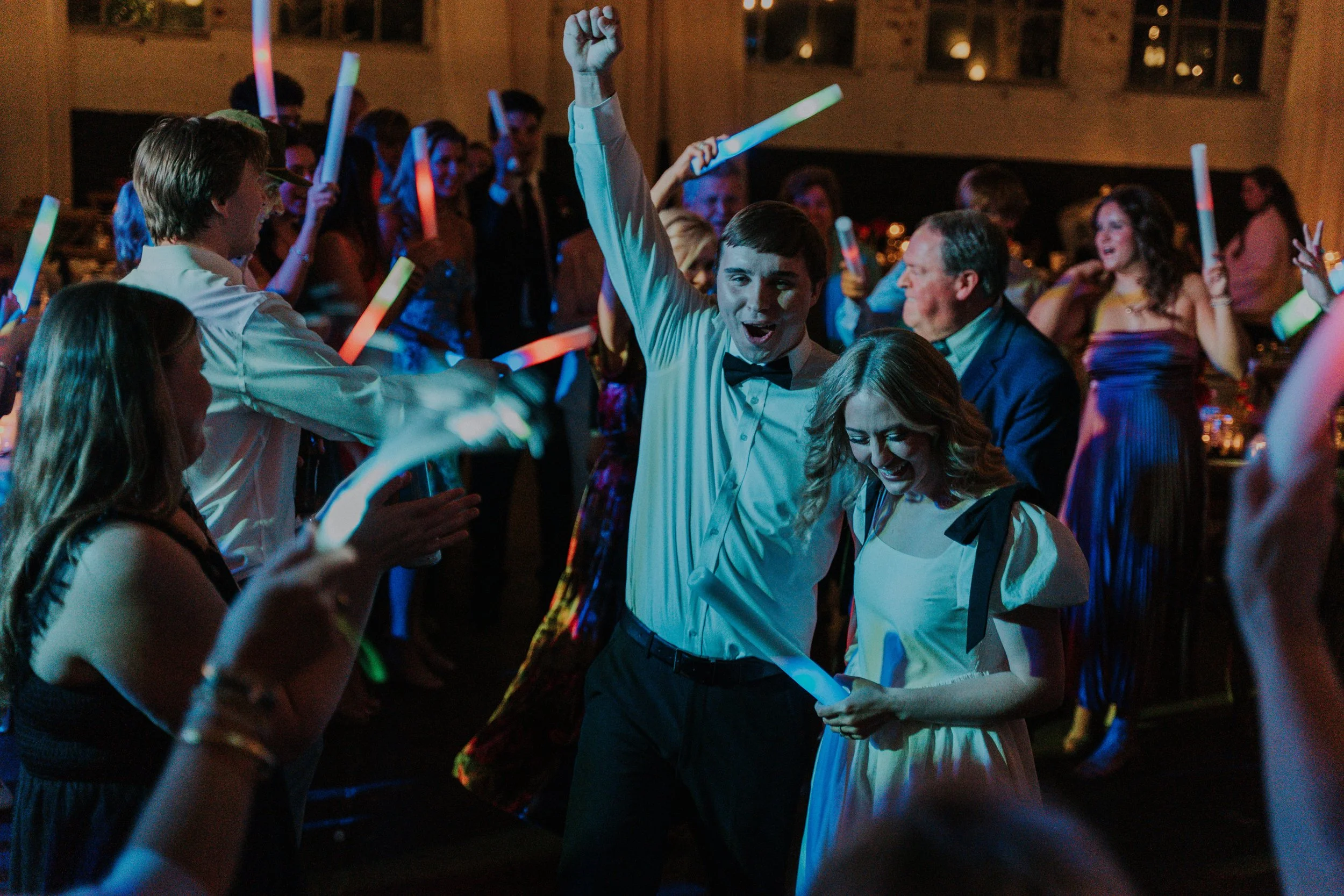 Celebration at a party with people dancing, waving glow sticks, and having fun in a dimly lit room.