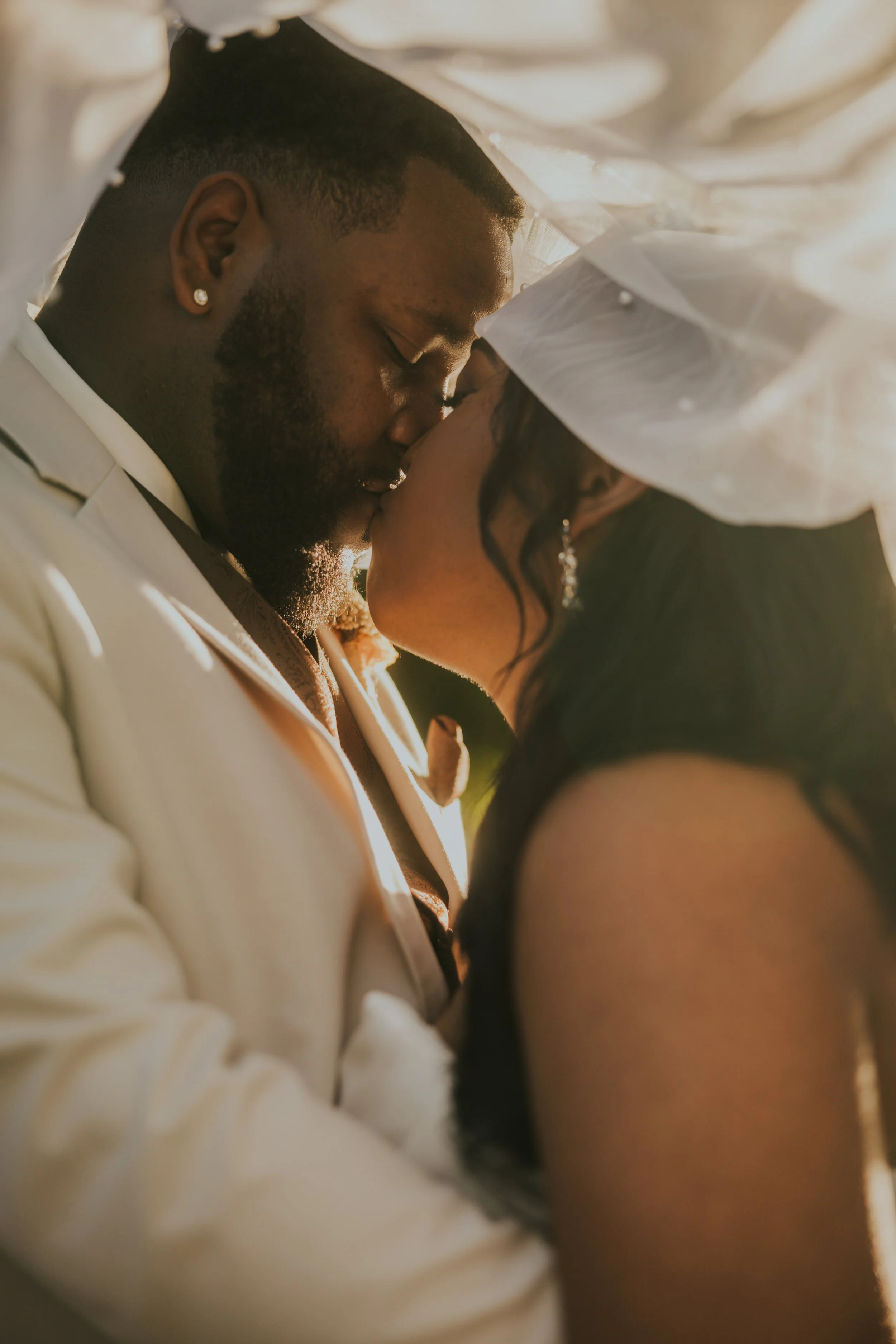 A couple kissing during a wedding, with warm lighting and the bride wearing a veil and earrings.