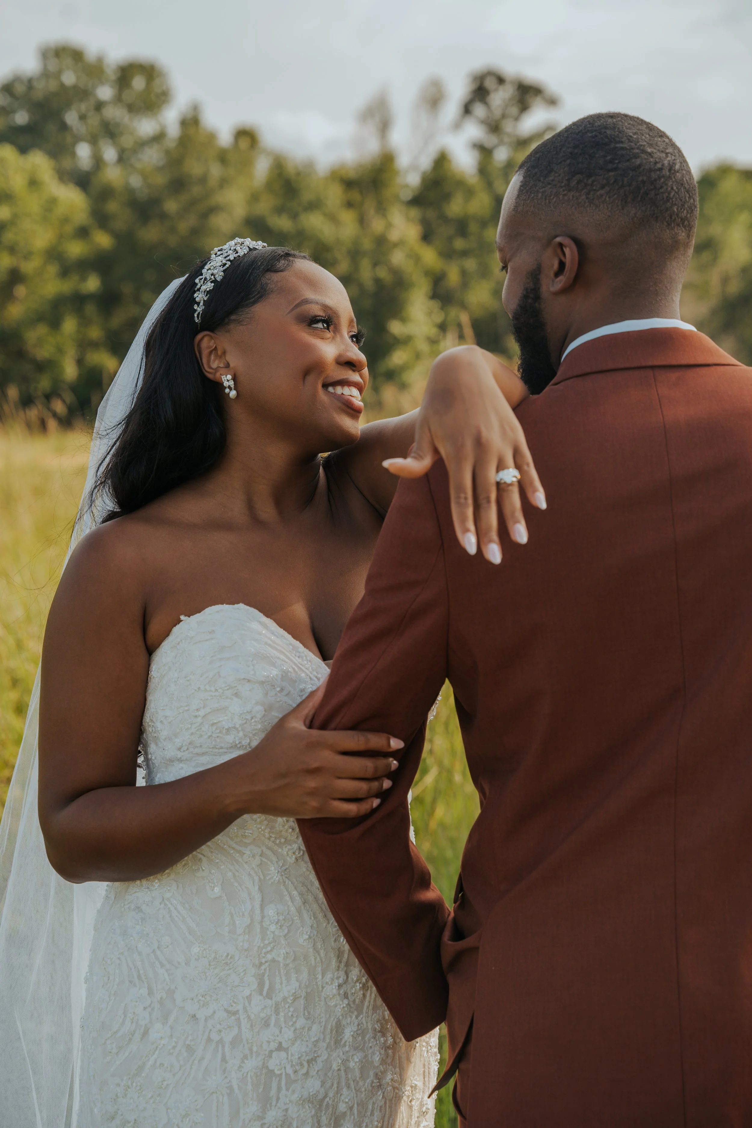 A bride and groom sharing an intimate moment outdoors, with the bride smiling and resting her arm on the groom's shoulder in a natural setting.