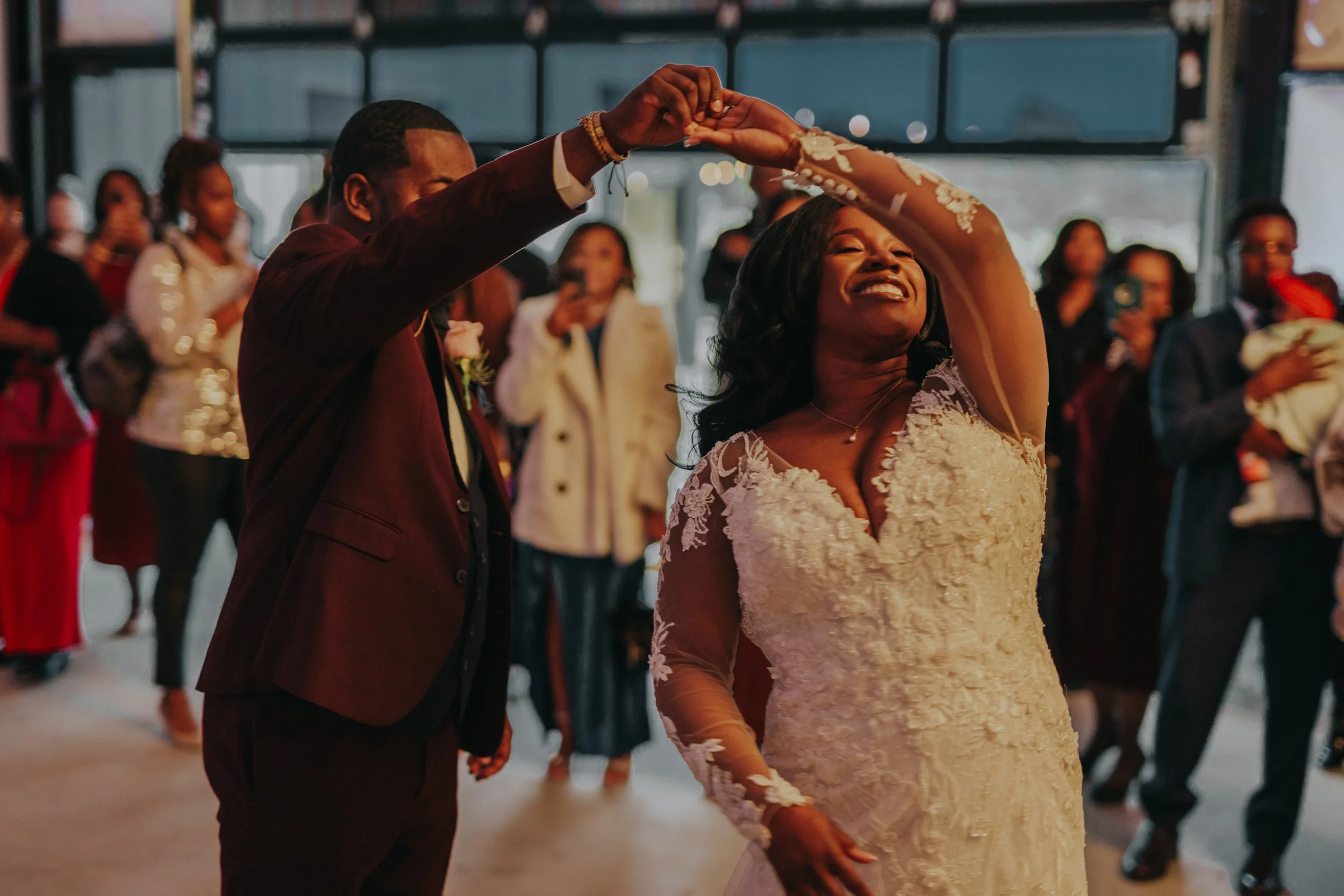 A joyful bride and groom dance at their wedding reception, surrounded by guests.