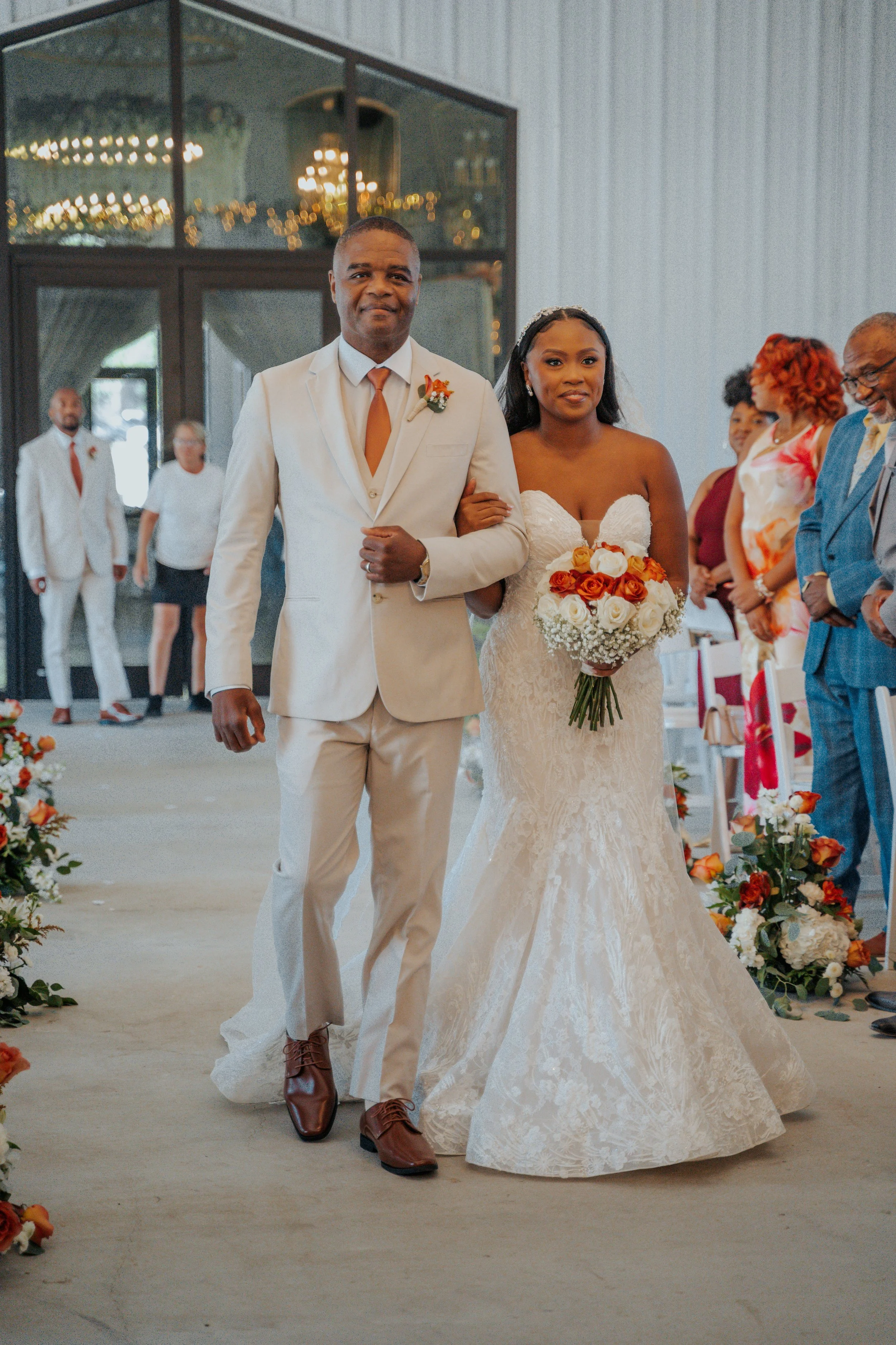 Bride walking down the aisle with her father during a wedding ceremony, surrounded by guests and floral decorations.