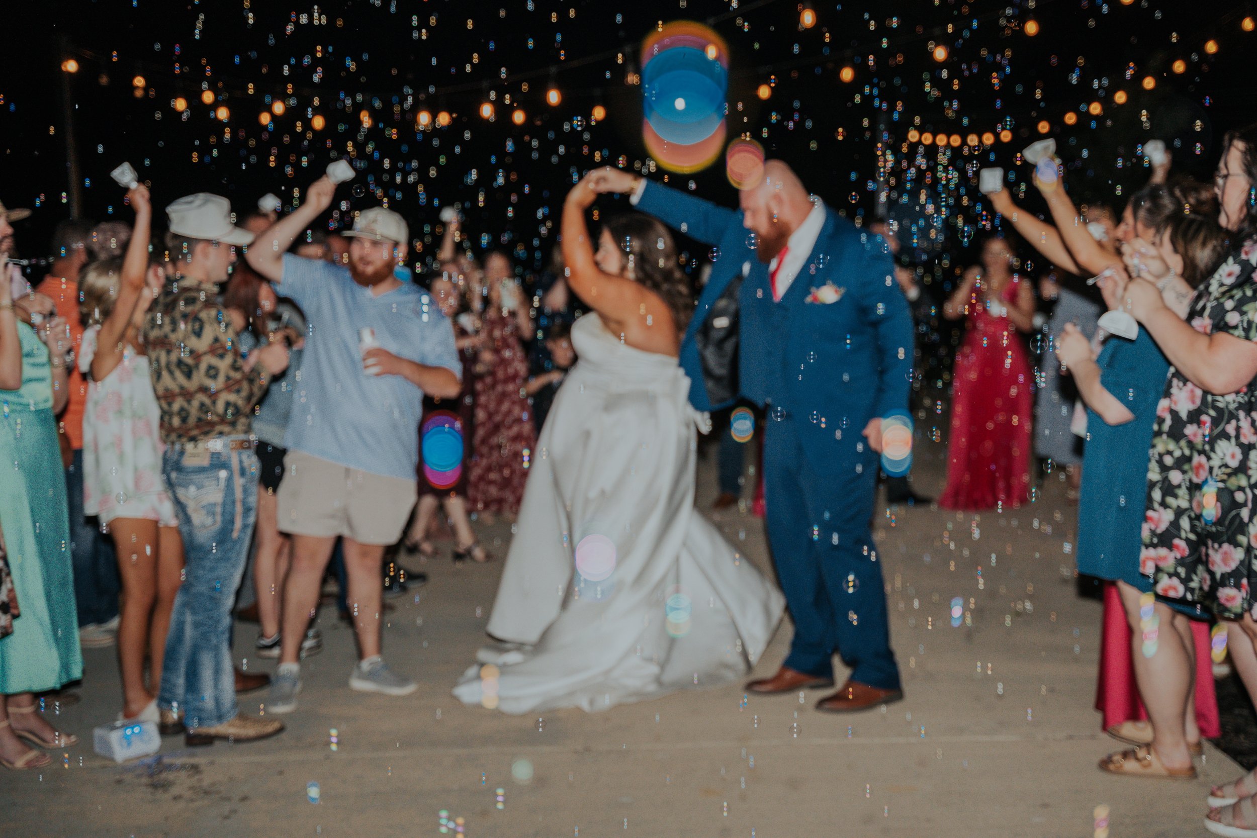 A bride and groom dance at their wedding reception with guests surrounding them under string lights at night.