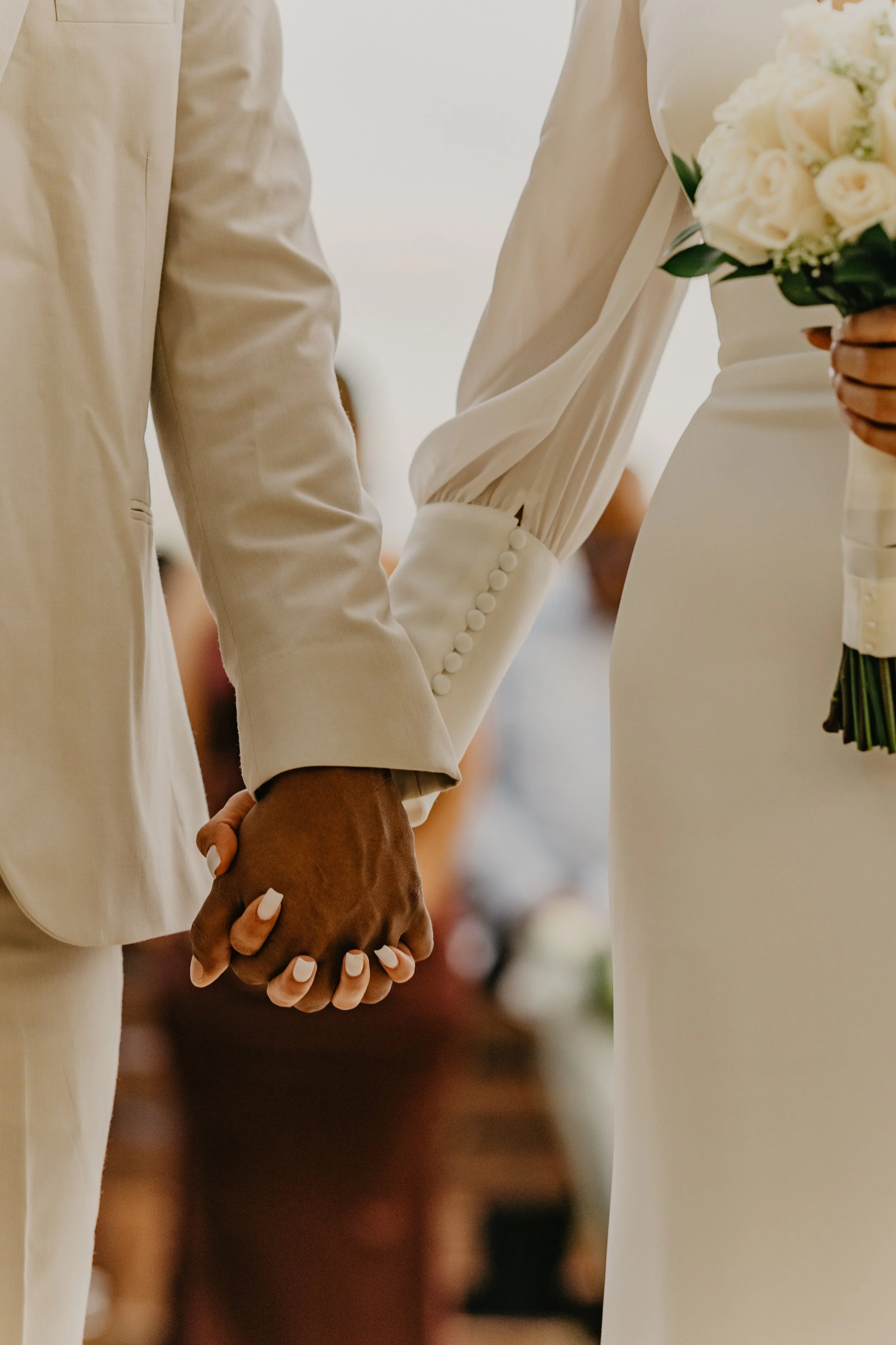 A bride and groom holding hands during a wedding ceremony, with the bride holding a bouquet of white roses.