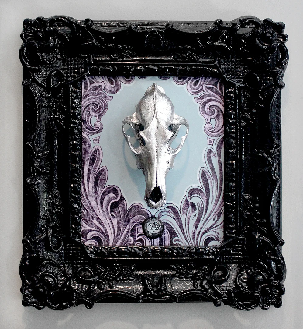 Title: STRIVE This is latest piece in the series of a new direction that Anthony is artistically heading. He is working on a unique fusion of painting, drawing and re-purposed objects. This piece features an authentic coyote skull that has been hand painted and silver leafed, mounted on a hand painted acrylic/mixed media background, and framed in a hand painted antique frame. The skulls that he acquires come from humane and environmentally responsible means. Adding to the flair, is the custom made wax stamp signature you will find on each painting. Each wax stamp has it's own unique design that is specific to the year the piece was created. This piece has been professionally framed and mounted with a dust cover and installed hanging hardware. 16"W X 18"H X 3.5"D SOLD