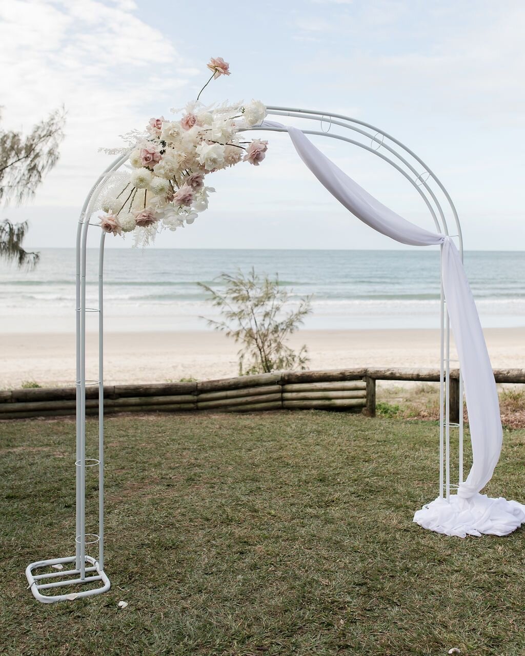 Michelle &amp; Gavin had a beautiful beachfront ceremony, featuring a stunning white arch abor with a muslin swag.

🤍 Wedding Details: 🤍

Planner/Stylist: @splashevents 
Photography: @katerobinson.co 
Venue: @sailsbeachnoosa 
Florals: @mapleflowers