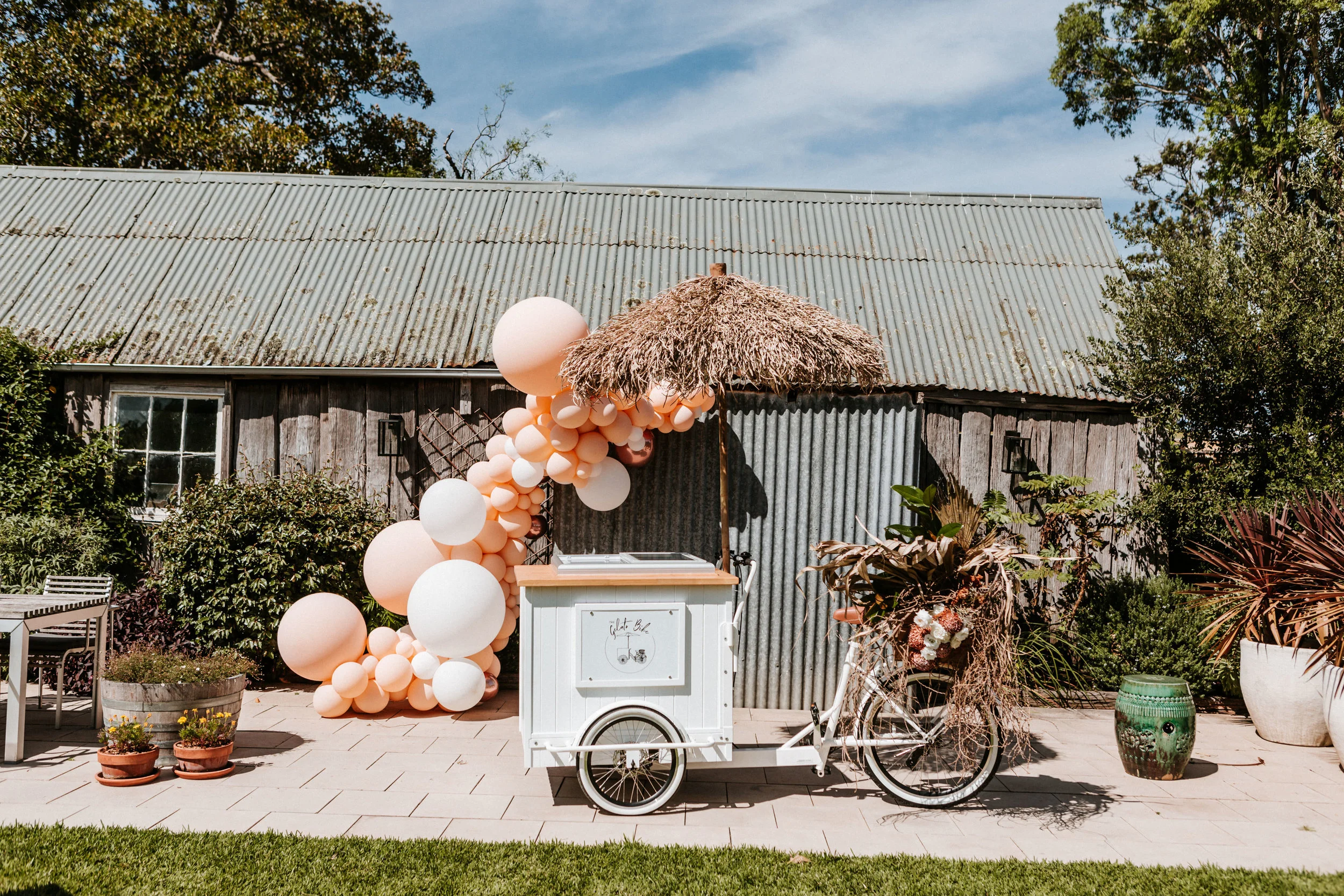 White gelato bike with seagrass umbrella and balloon garland for wedding styling