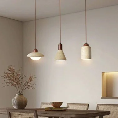 Three travertine stone pendant lights in dome, cone and cylinder shapes hanging over a wooden dining table