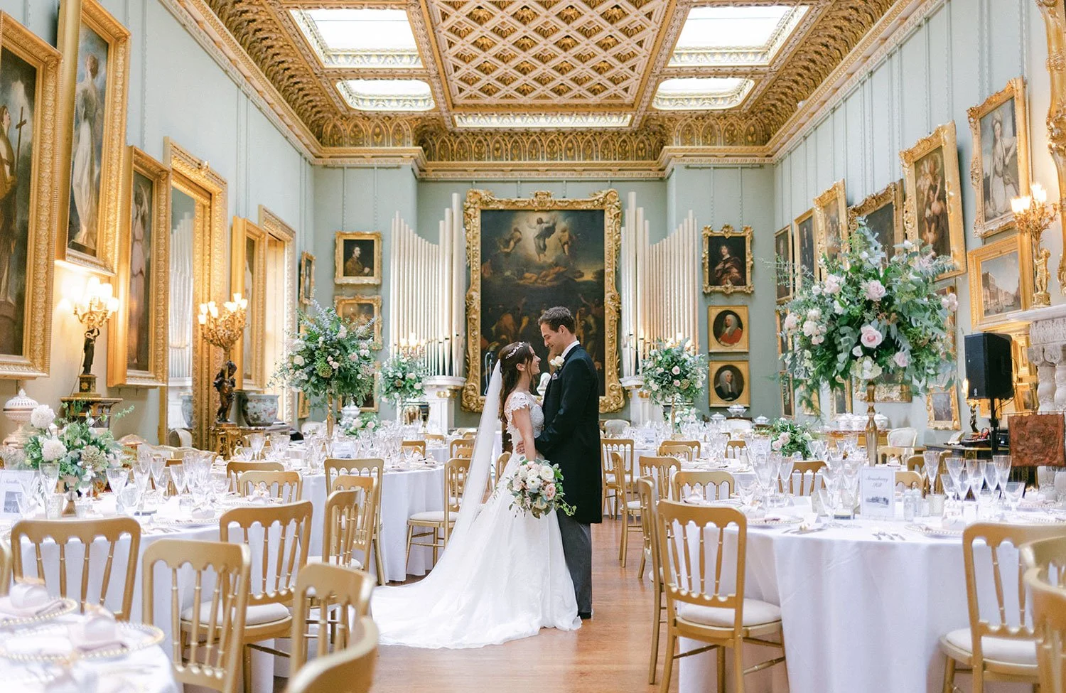 A Bride and Groom hold hands in a room full of stunning fresh wedding flowers.