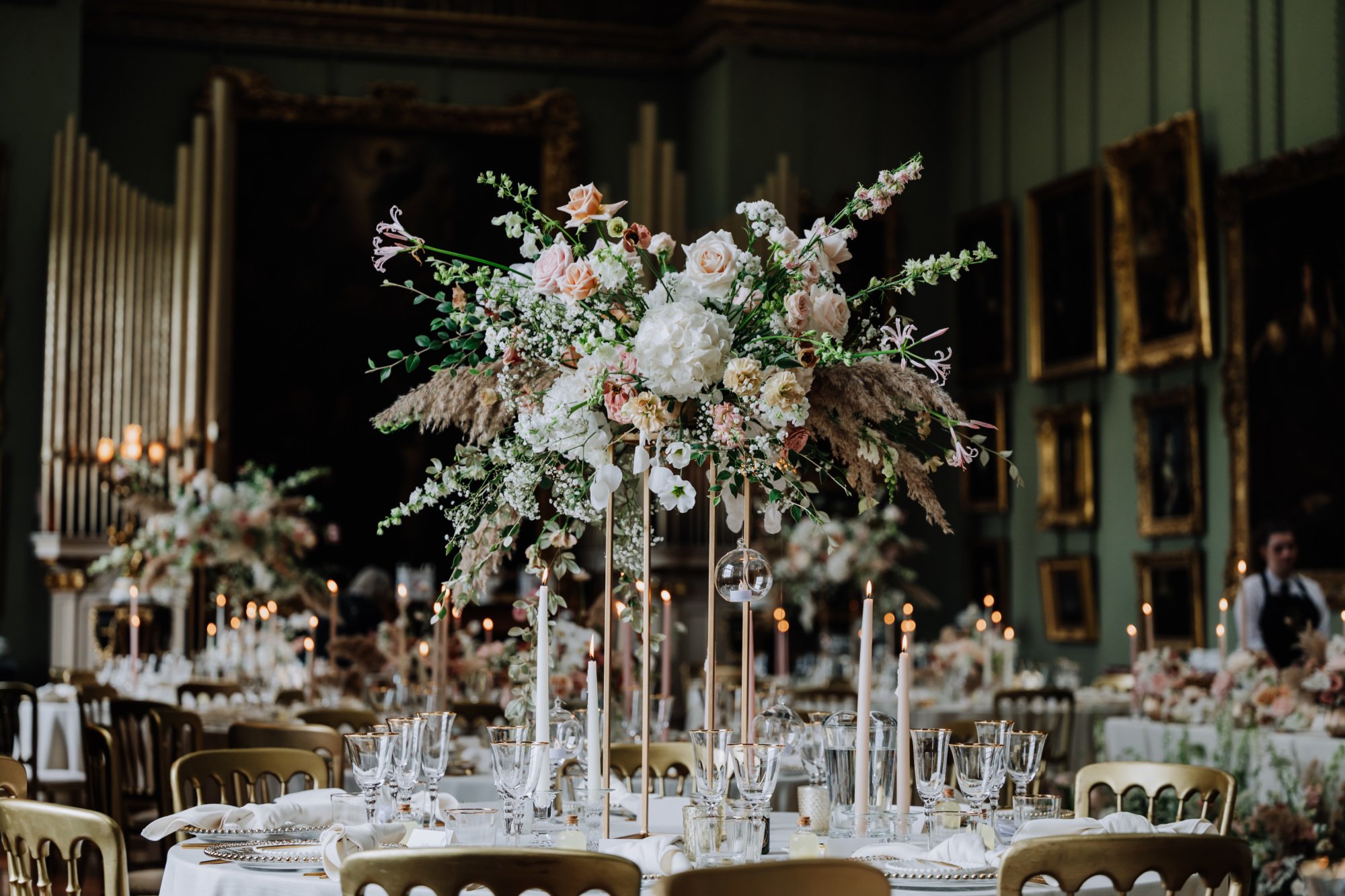 A grand banquet hall decorated with beautiful wedding flowers with white tablecloths, glassware, and candles.