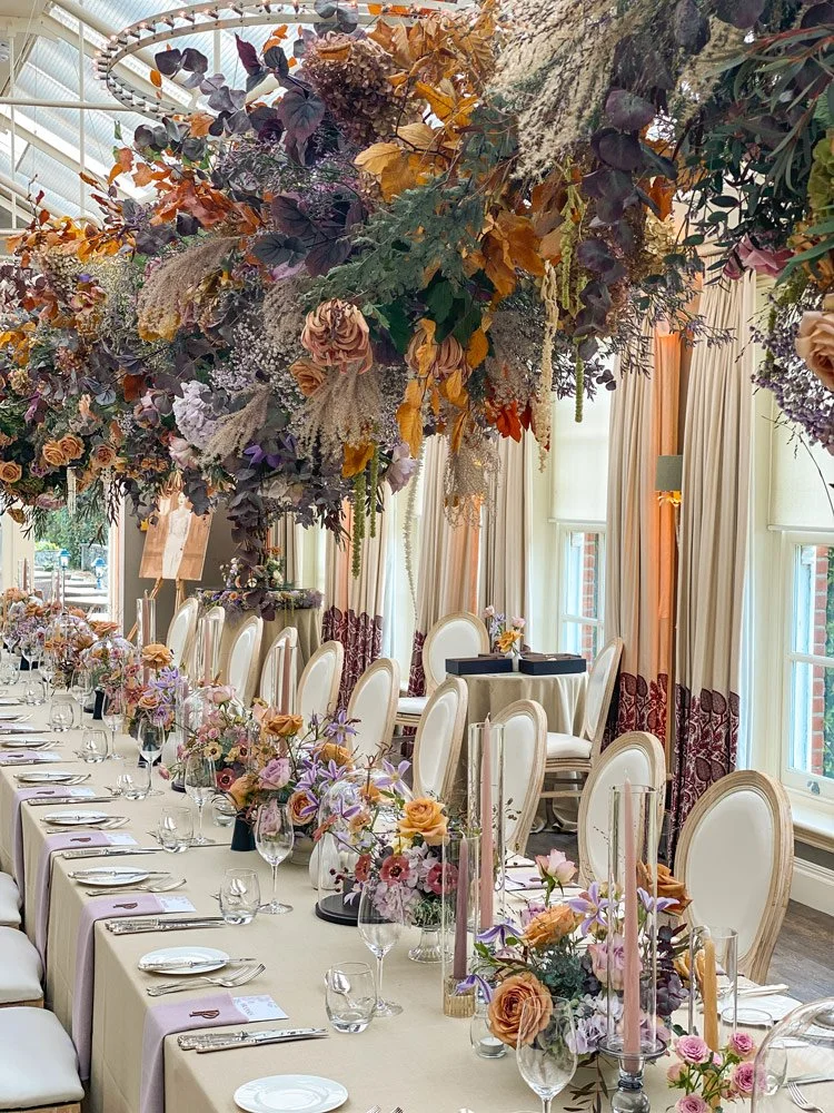 Elegant wedding table setting with floral arrangements and cascading floral ceiling installation in a decorated room.