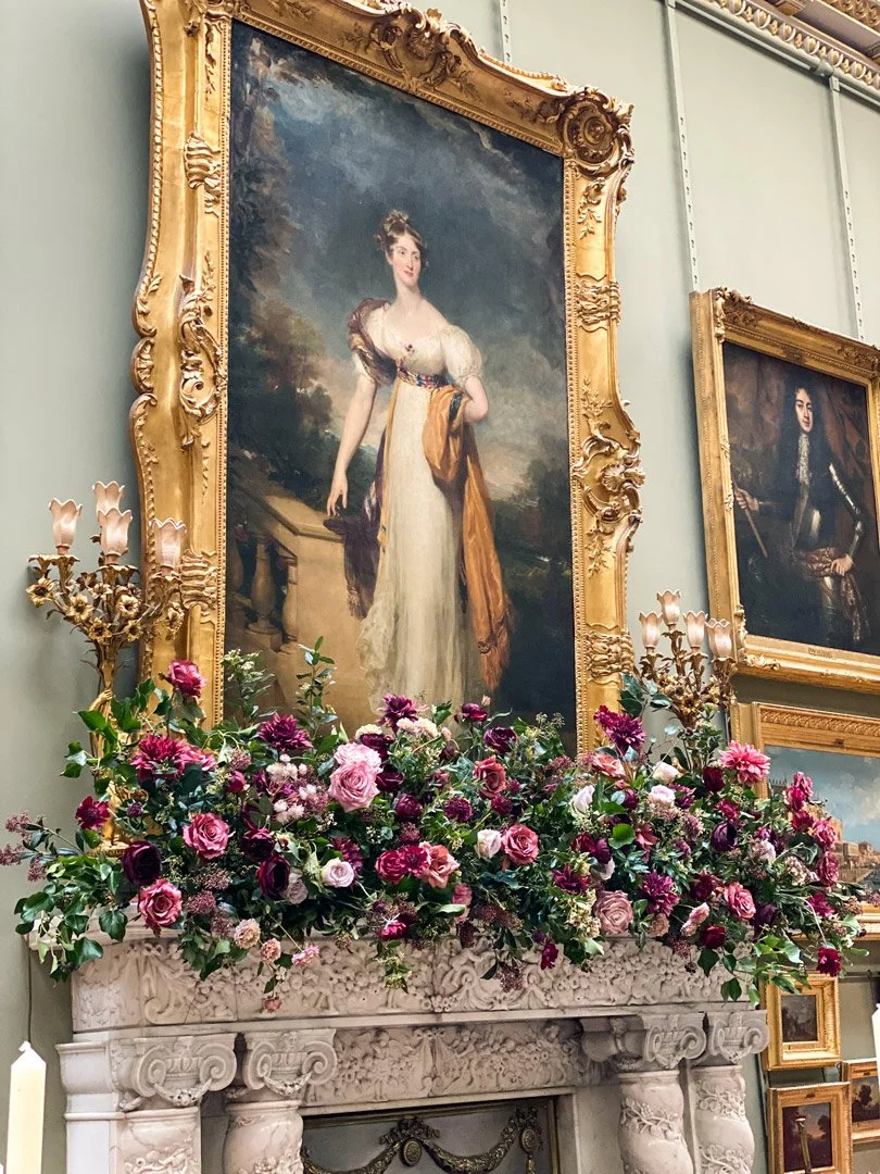 A decorated stone fireplace with a large bouquet of pink and purple flowers and two ornate gold-colored candelabra on either side.