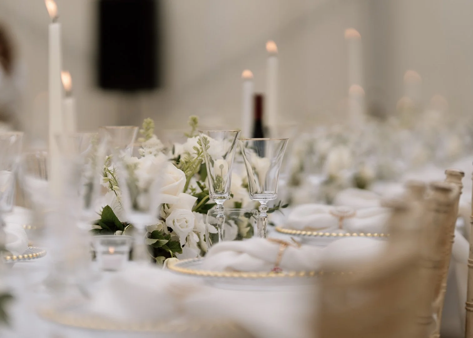 Elegant table setting with white floral centerpiece, glassware, plates, and candles for a formal event or wedding reception.