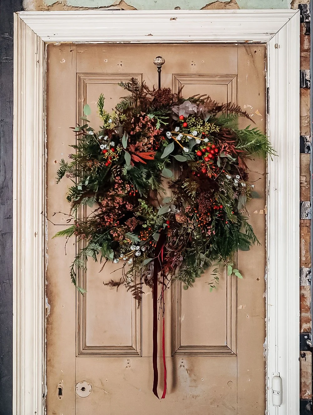 Large handcrafted Christmas wreath displayed on a stylish front door with seasonal foliage