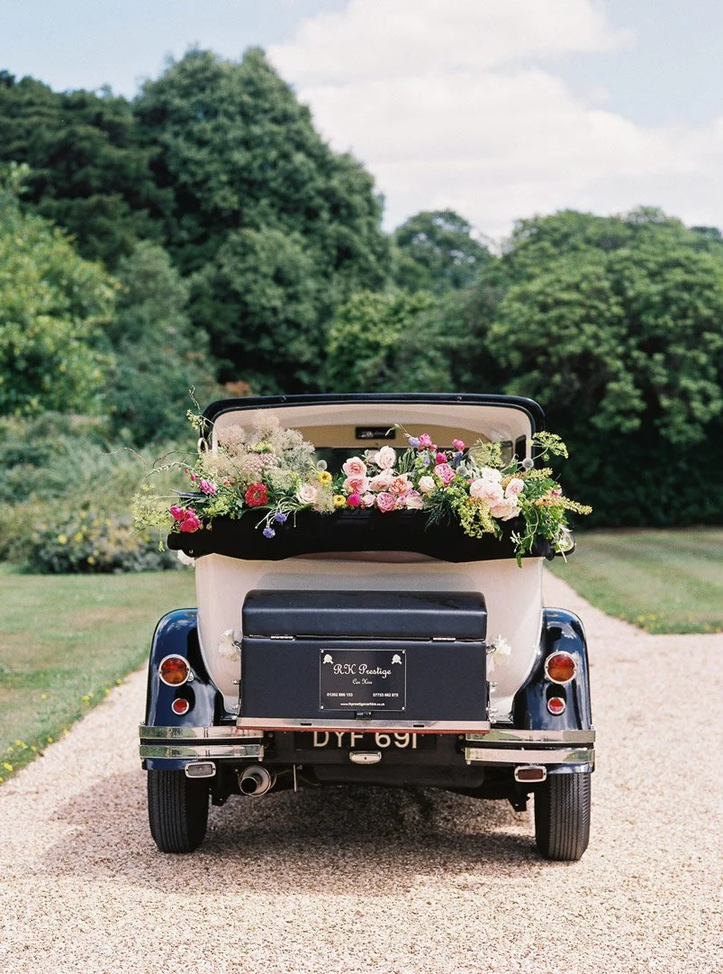 Vintage wedding car decorated with cascading flowers and silk ribbons
